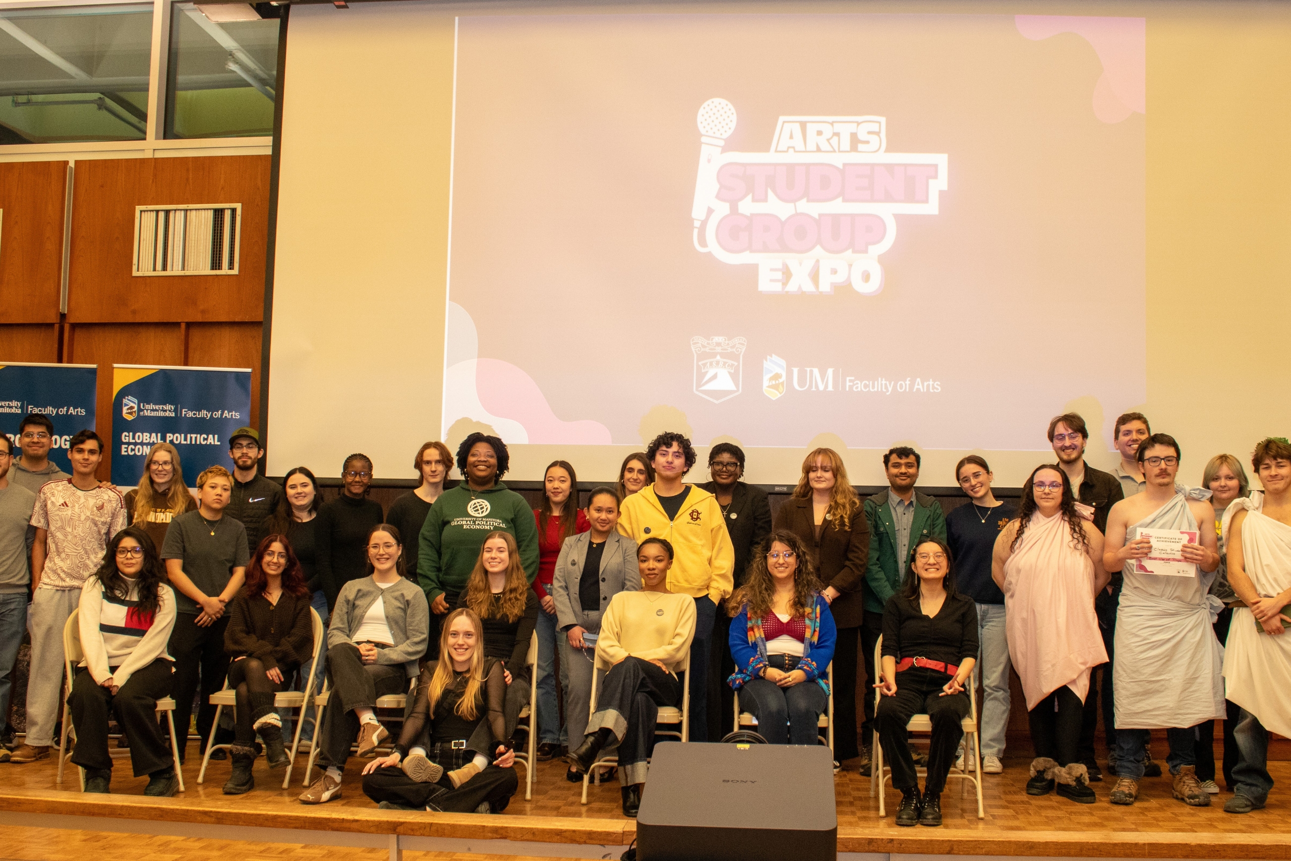 A group of over 50 students pose for the camera on stage.