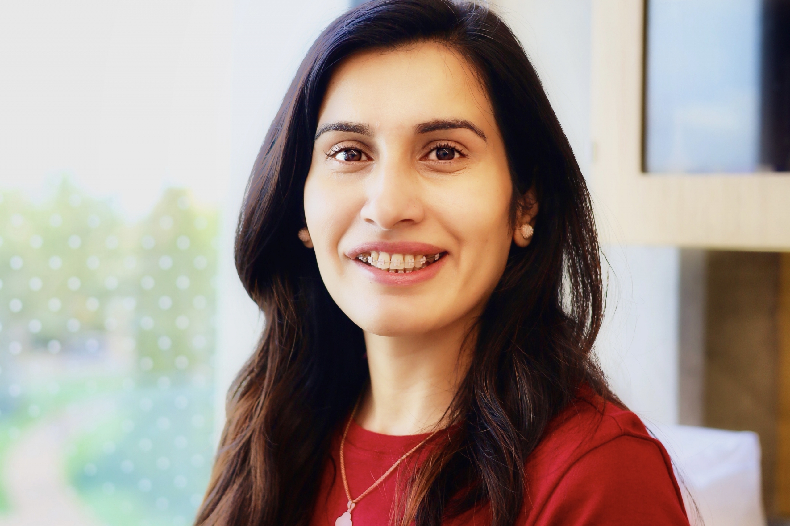 Portrait of Dr. Iqra Azam seated indoors, smiling at the camera and wearing a red top