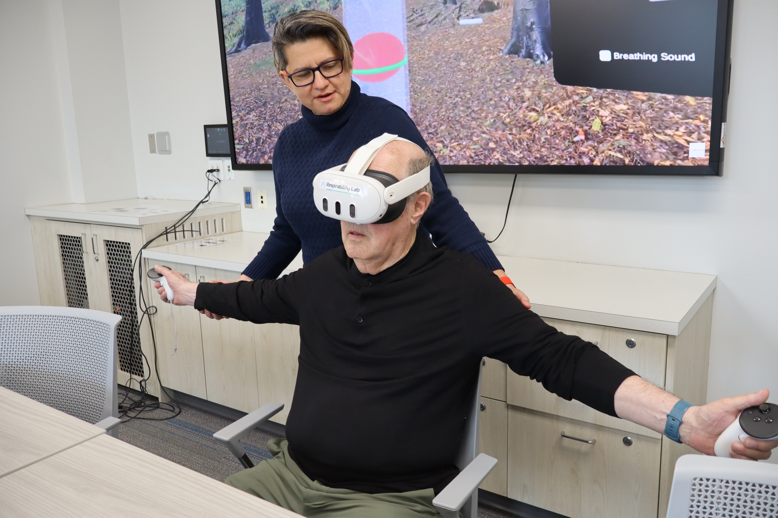 Diana Sanchez-Ramirez works with a patient researcher who is wearing a virtual reality headset.