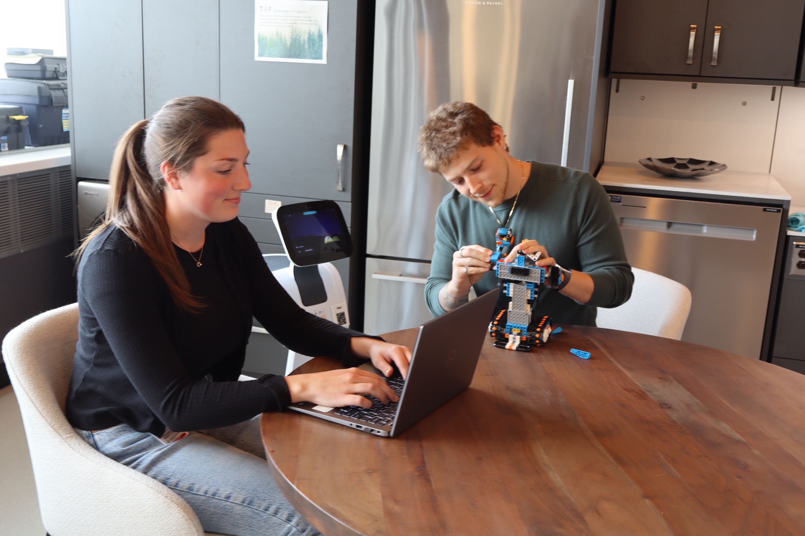 Student researchers Brooke Peerson and Seth Broder work with robots at a table in the TAL smart suite.