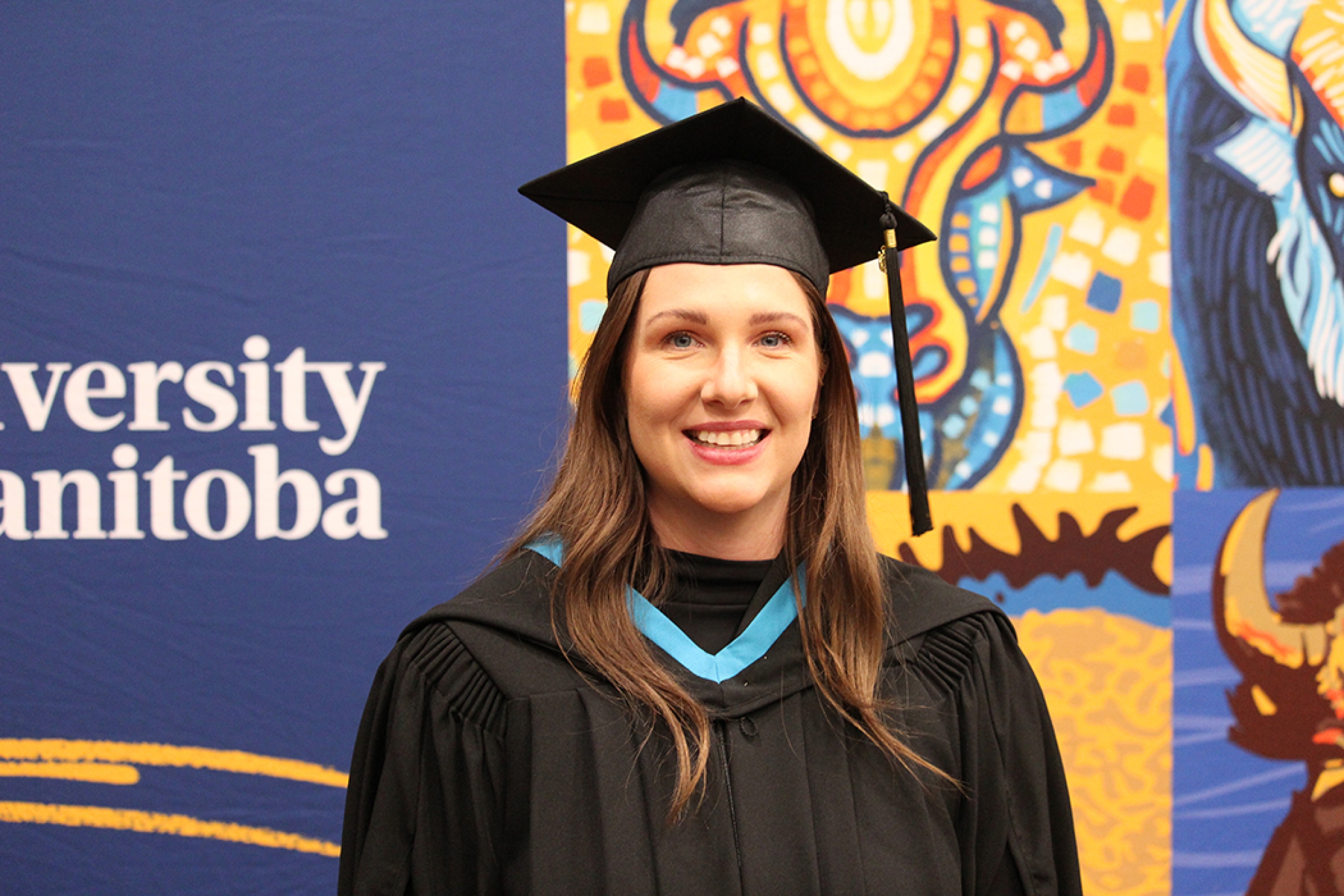 Jessica Smart stands in front of a University of Manitoba banner wearing a convocation cap and gown.
