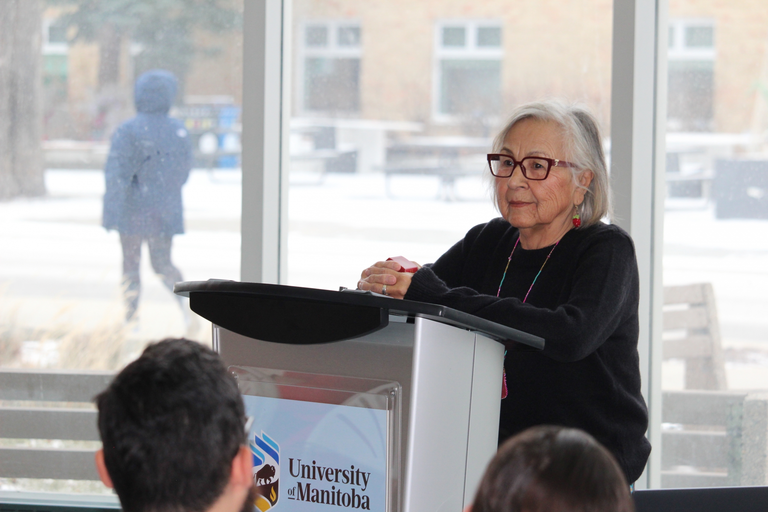 Margaret Lavallee speaks at a podium in front of a large window at Bannatyne Campus. at B