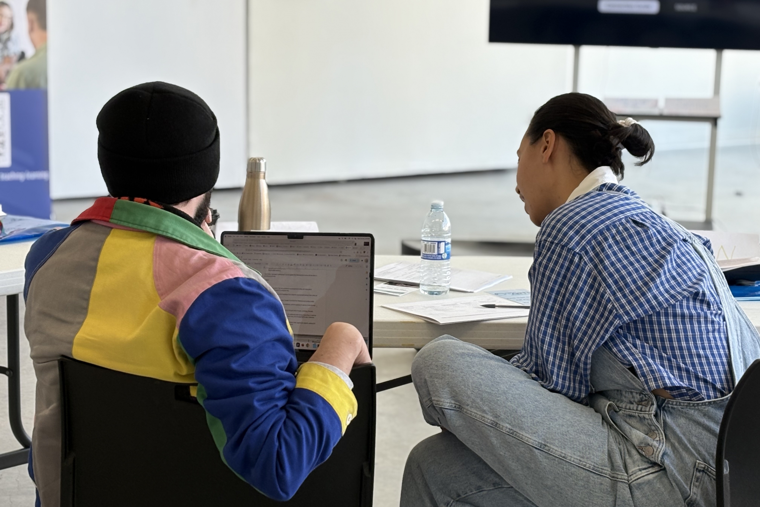 Two students sitting at a table looking at a laptop.
