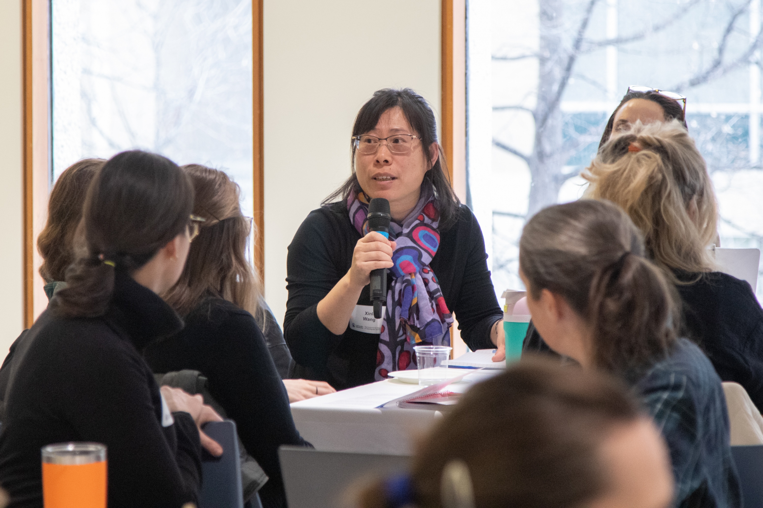 Dr. Xinli Wang holds a microphone and offers guidance in a group discussion