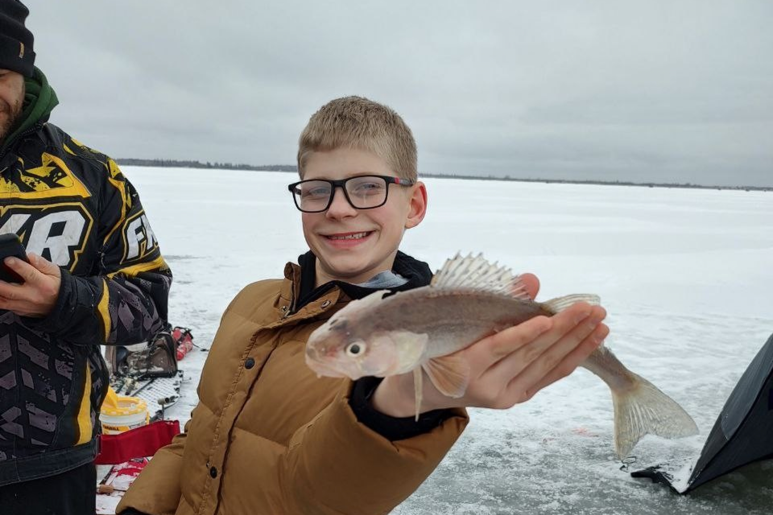 a young boy holds a fish on a frozen lake