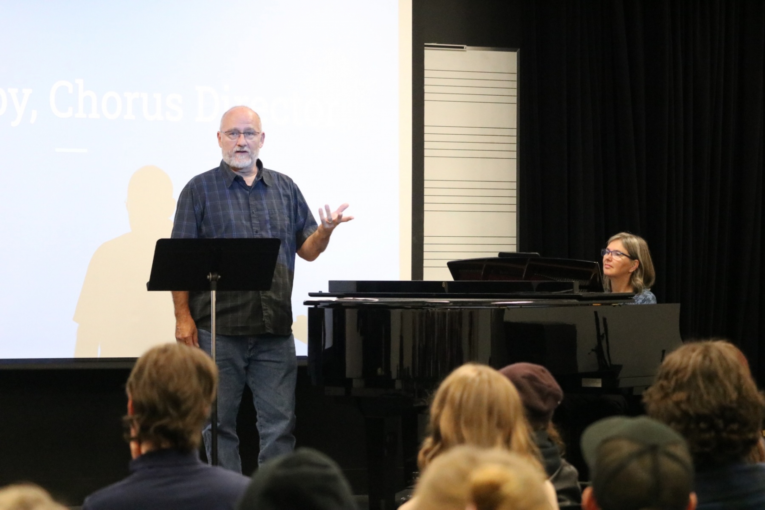 Man stands at a music podium in front of students.
