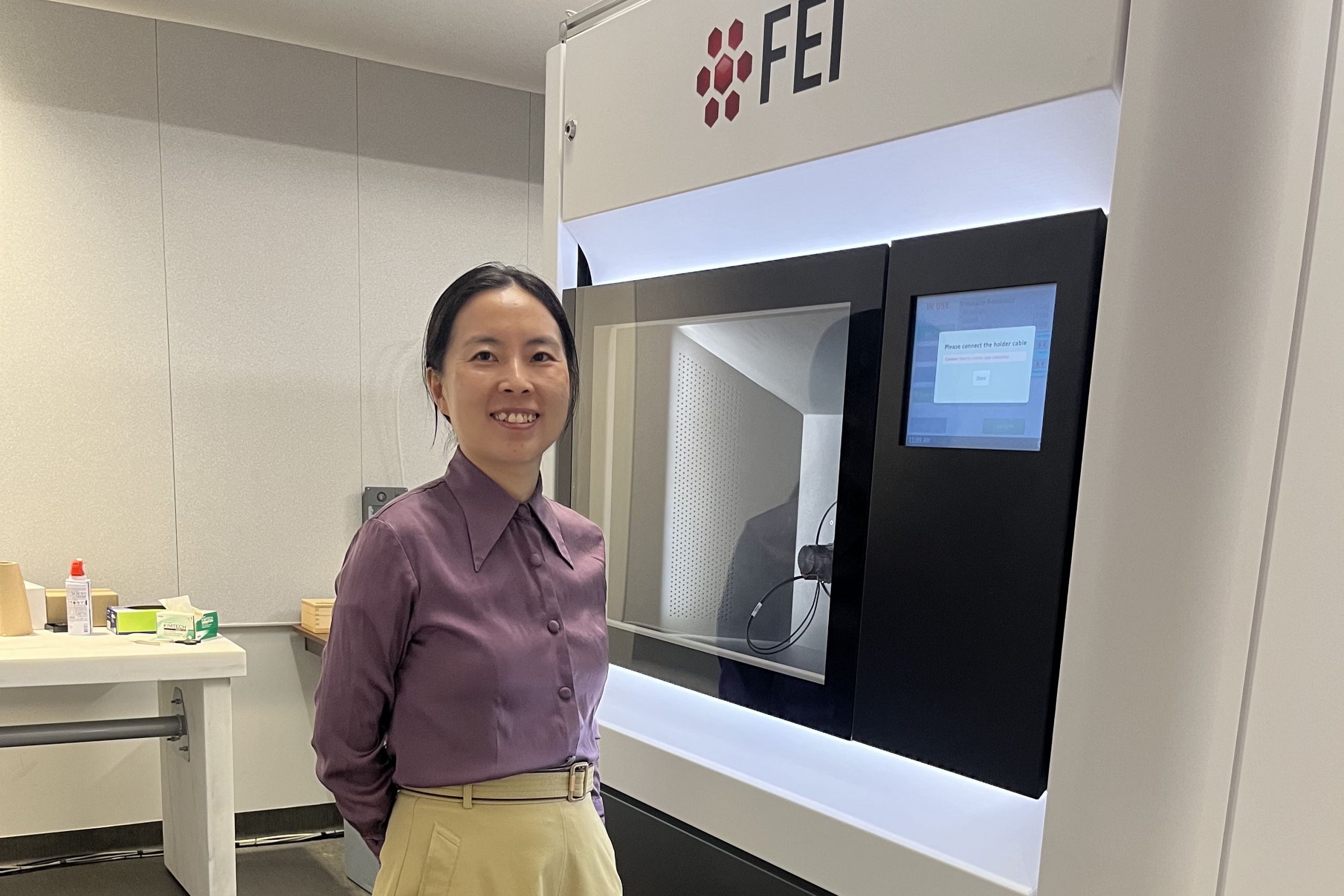 Guozhen Zhu standing beside an electron microscope