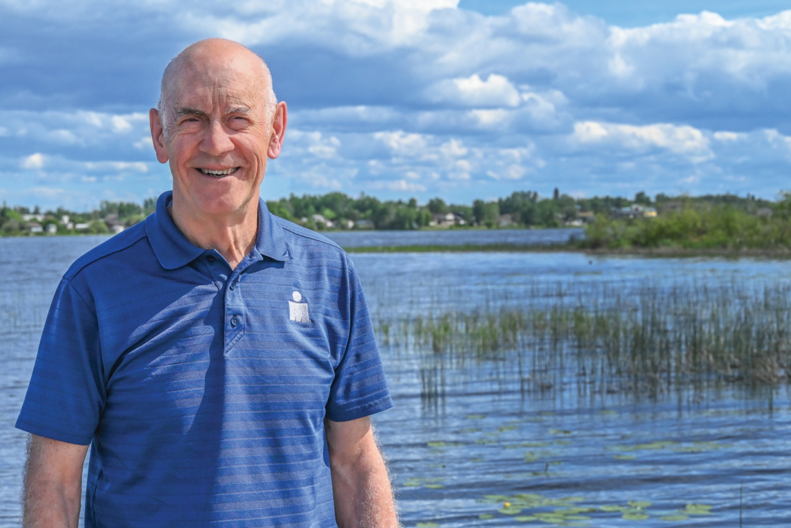 A person in front of a lake smiles at the camera.