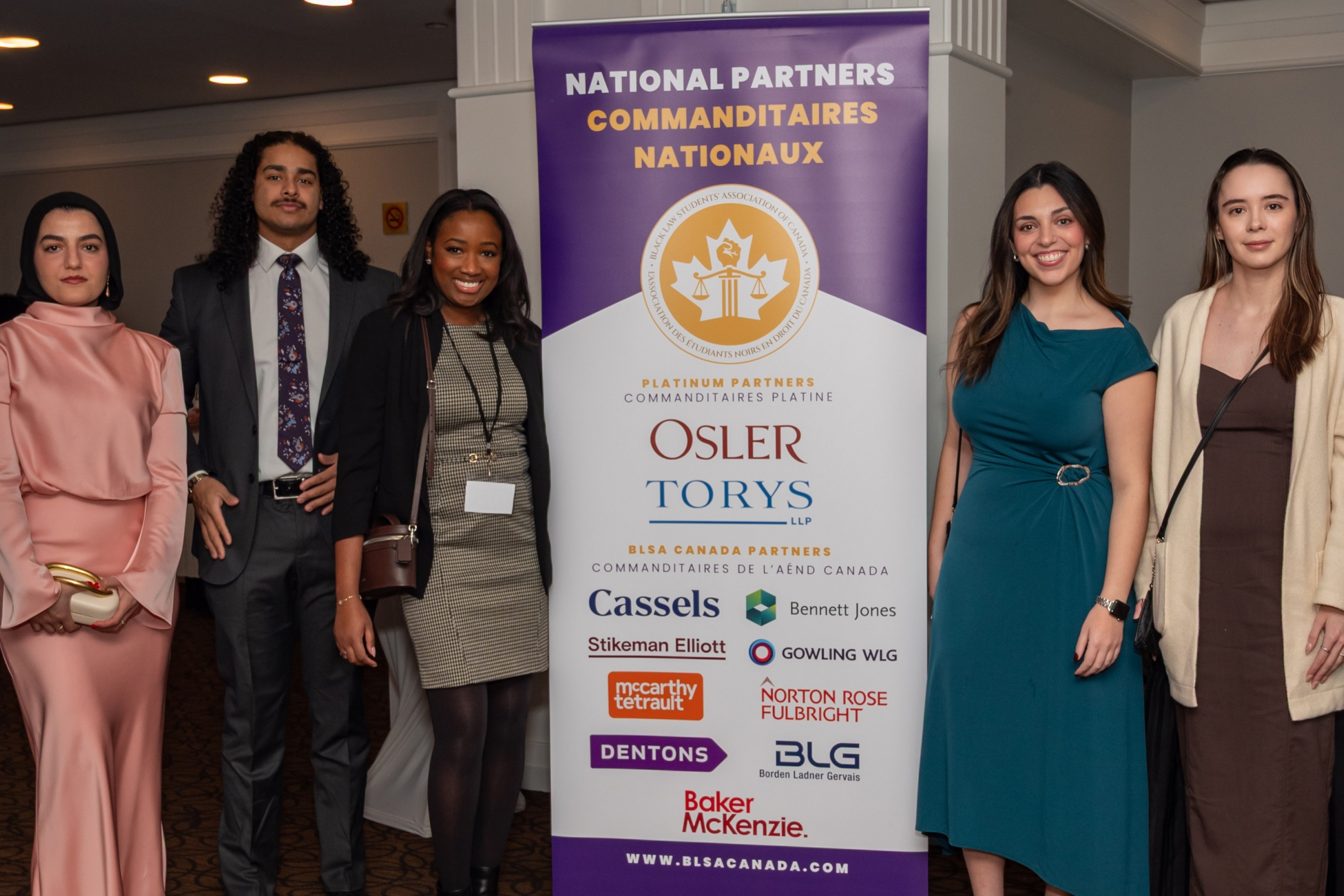 four law students and one moot team coach in formal wear pose in front of a roll up banner for the Black Law Students Association Isaac Moot sponsors