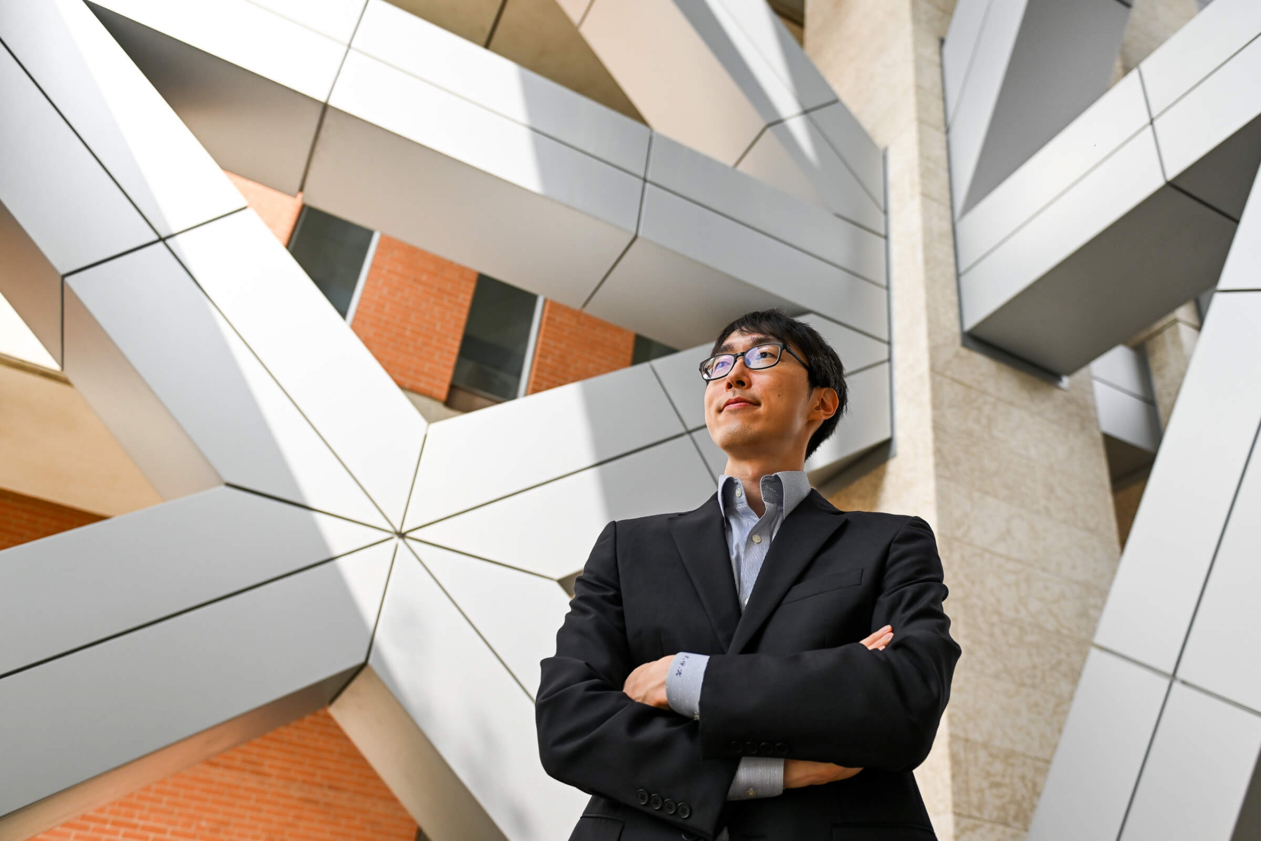 A man with glasses (Jae Yun Kim) wearing a suit in the lobby of a building