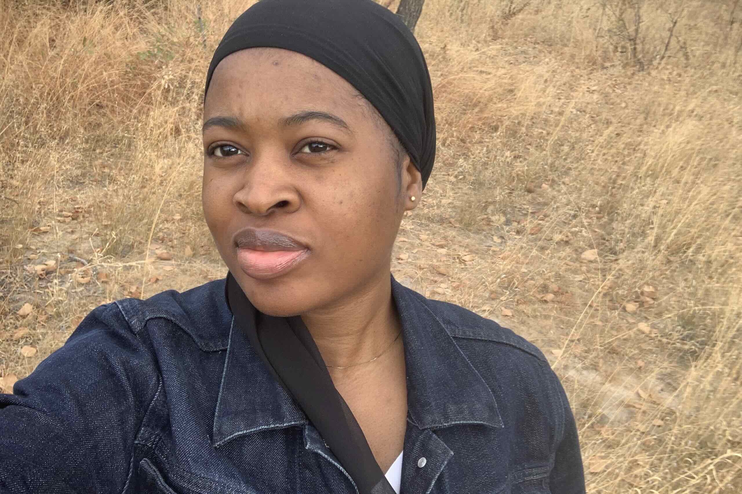 Selfie of black woman in jean jacket, with short, dry grasses in background.