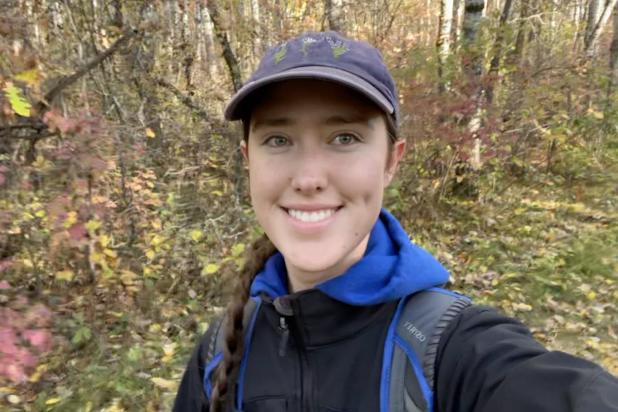 Smiling young woman wearing cap in a forest setting.