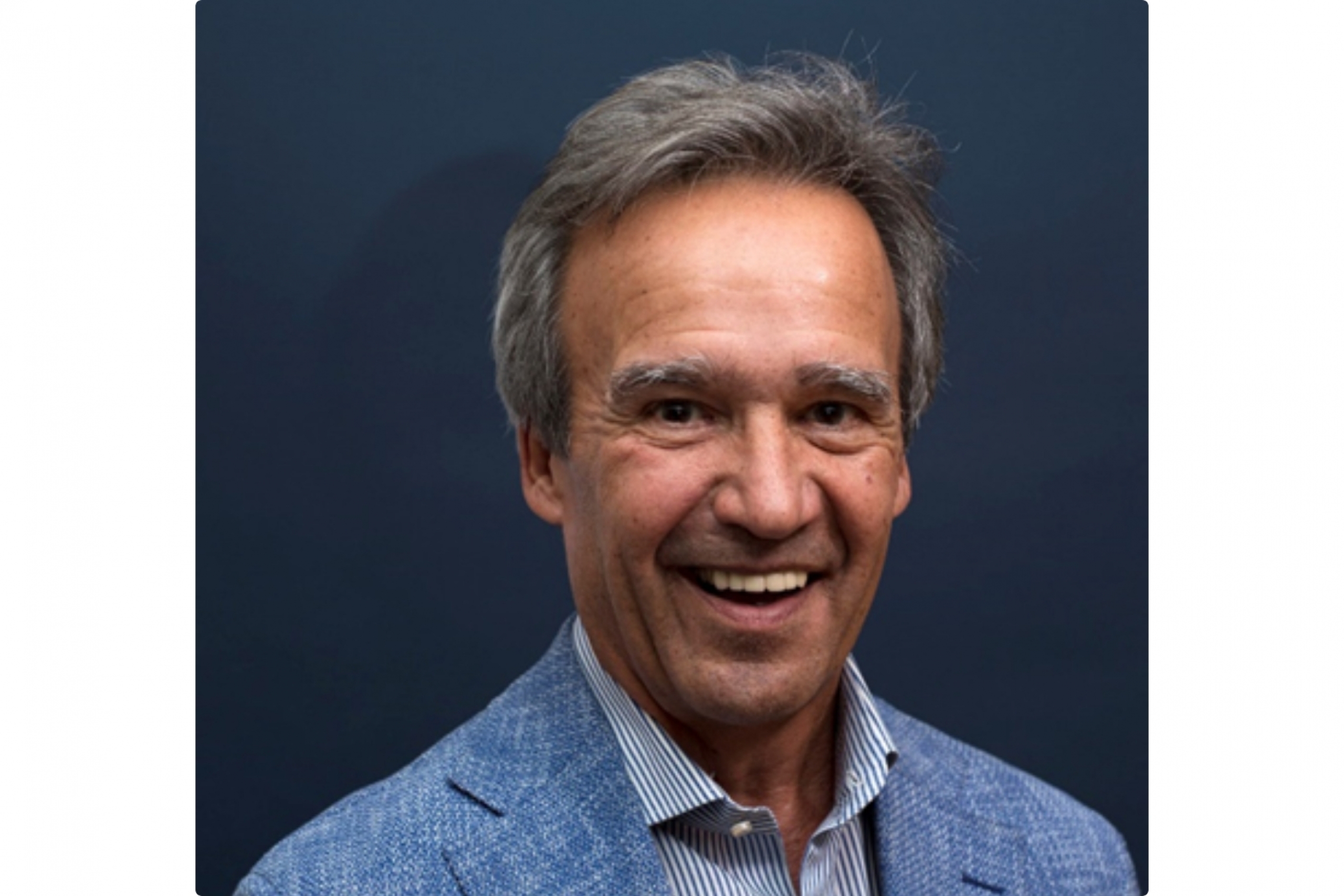 Man in a blue blazer smiling against a dark background.