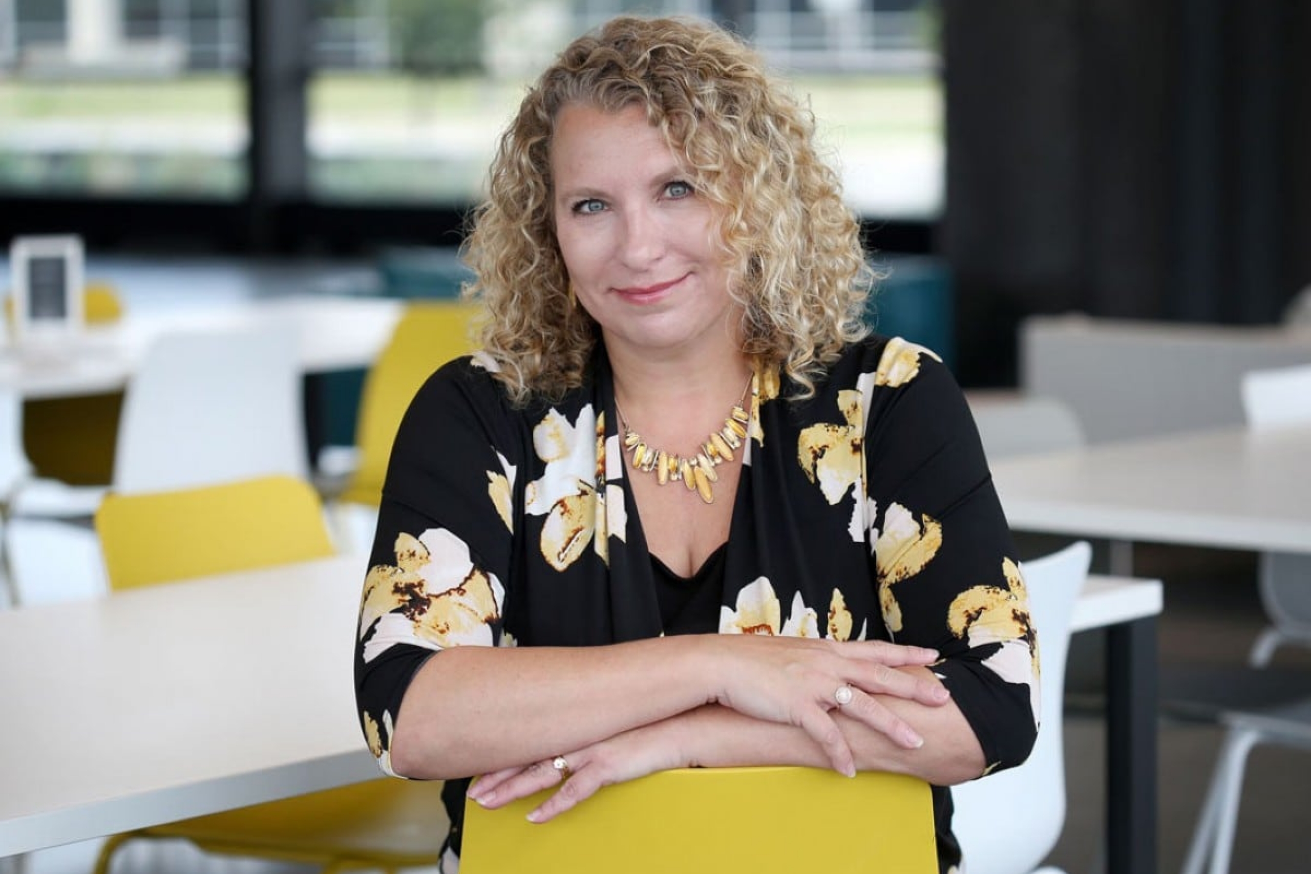 Woman seated at a table in a modern office setting.