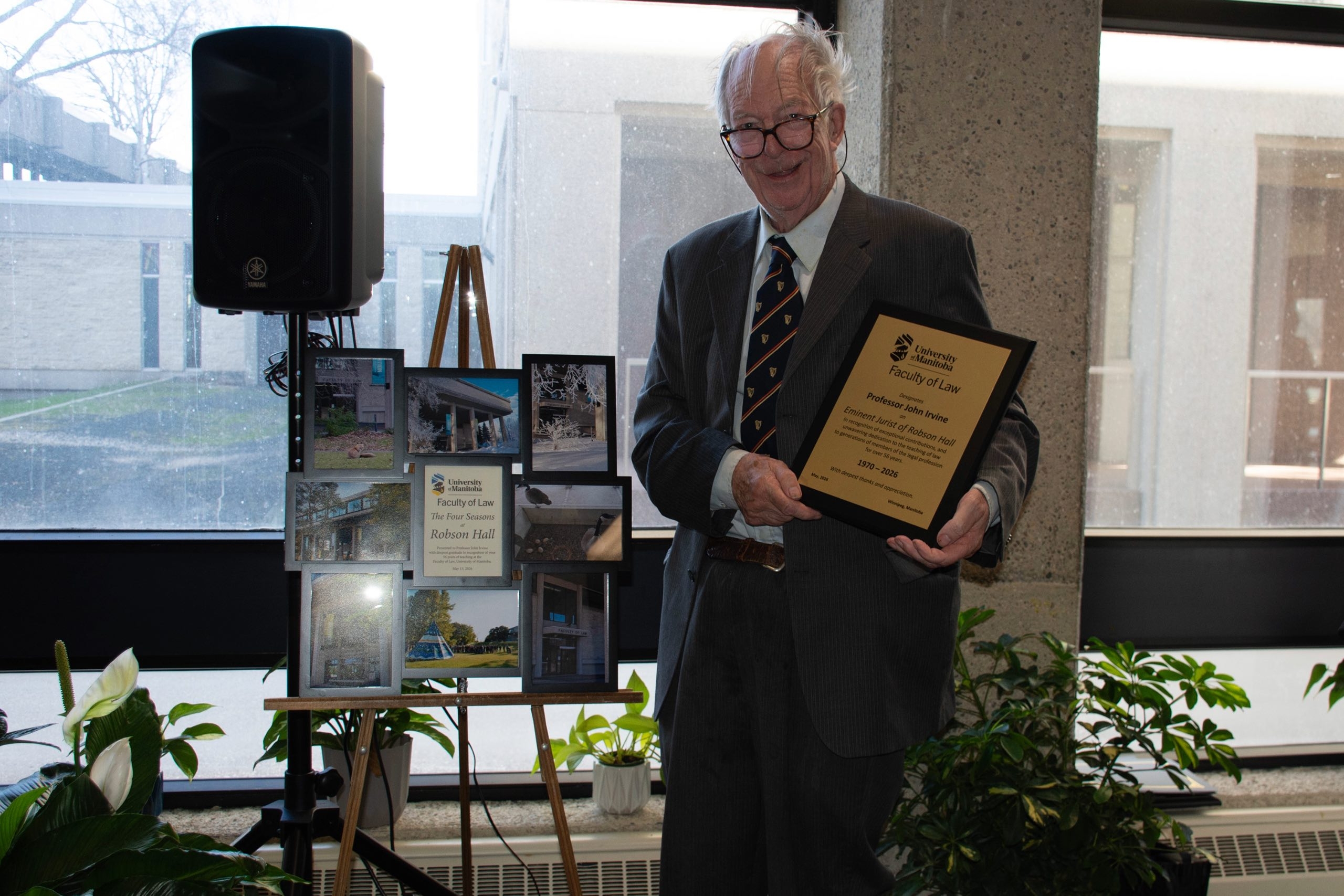 Professor John Irvine holds a plaque standing next to a collage of photos presented upon his retirement