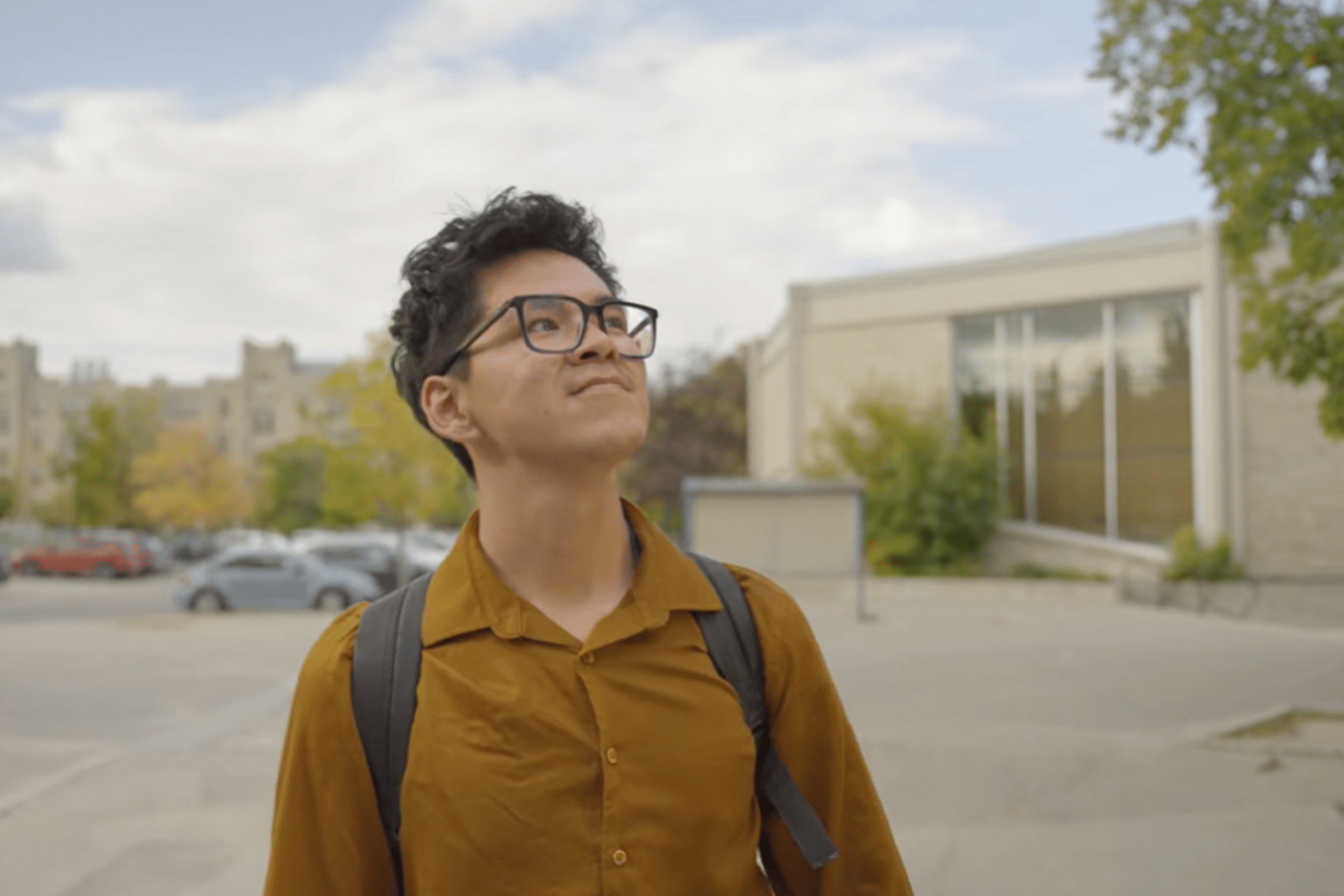 Josh looks upward with a smile while walking through campus on a summer day.