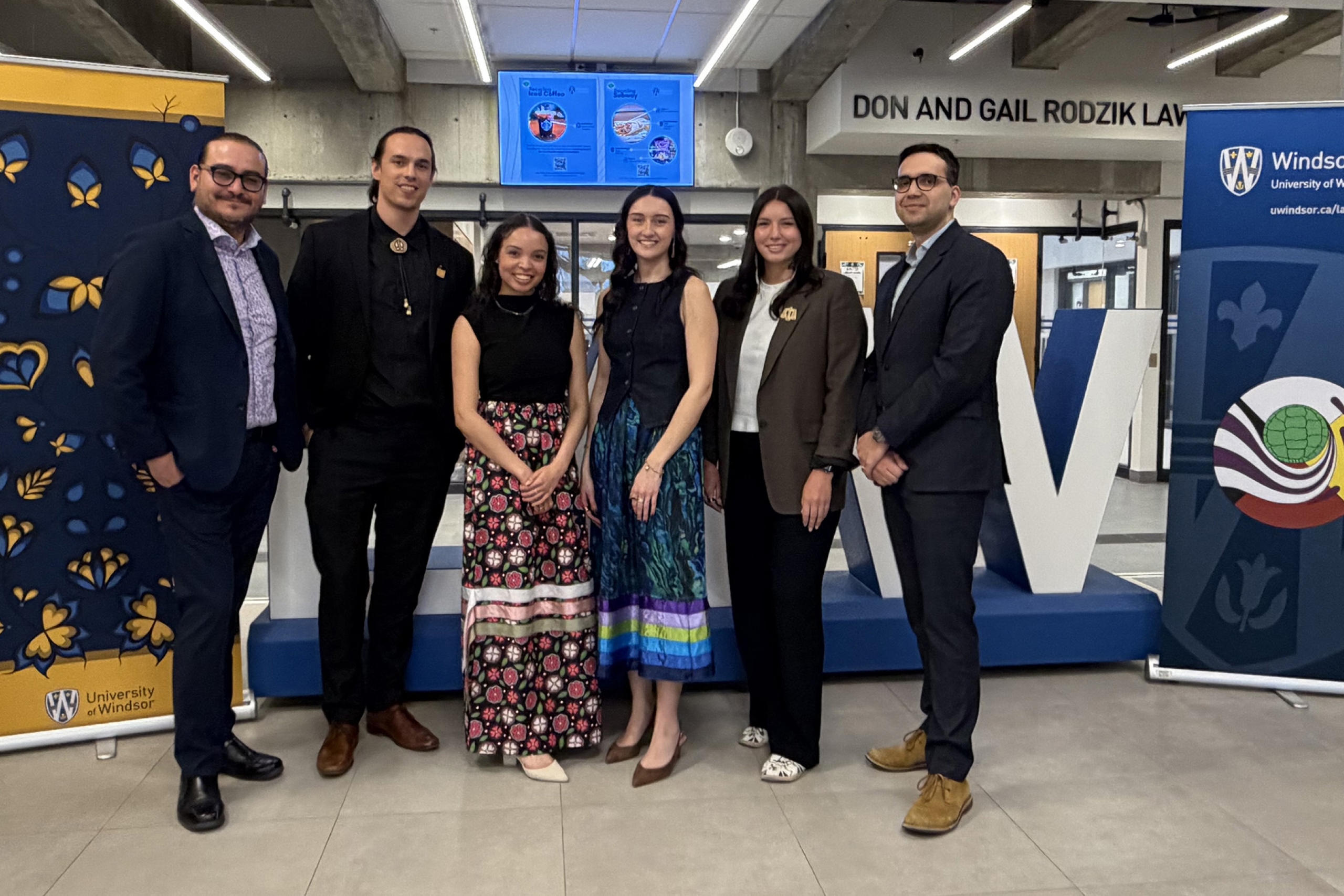 a group of law students and coaches stand in a hallway in front of banners wearing suits and formal wear.