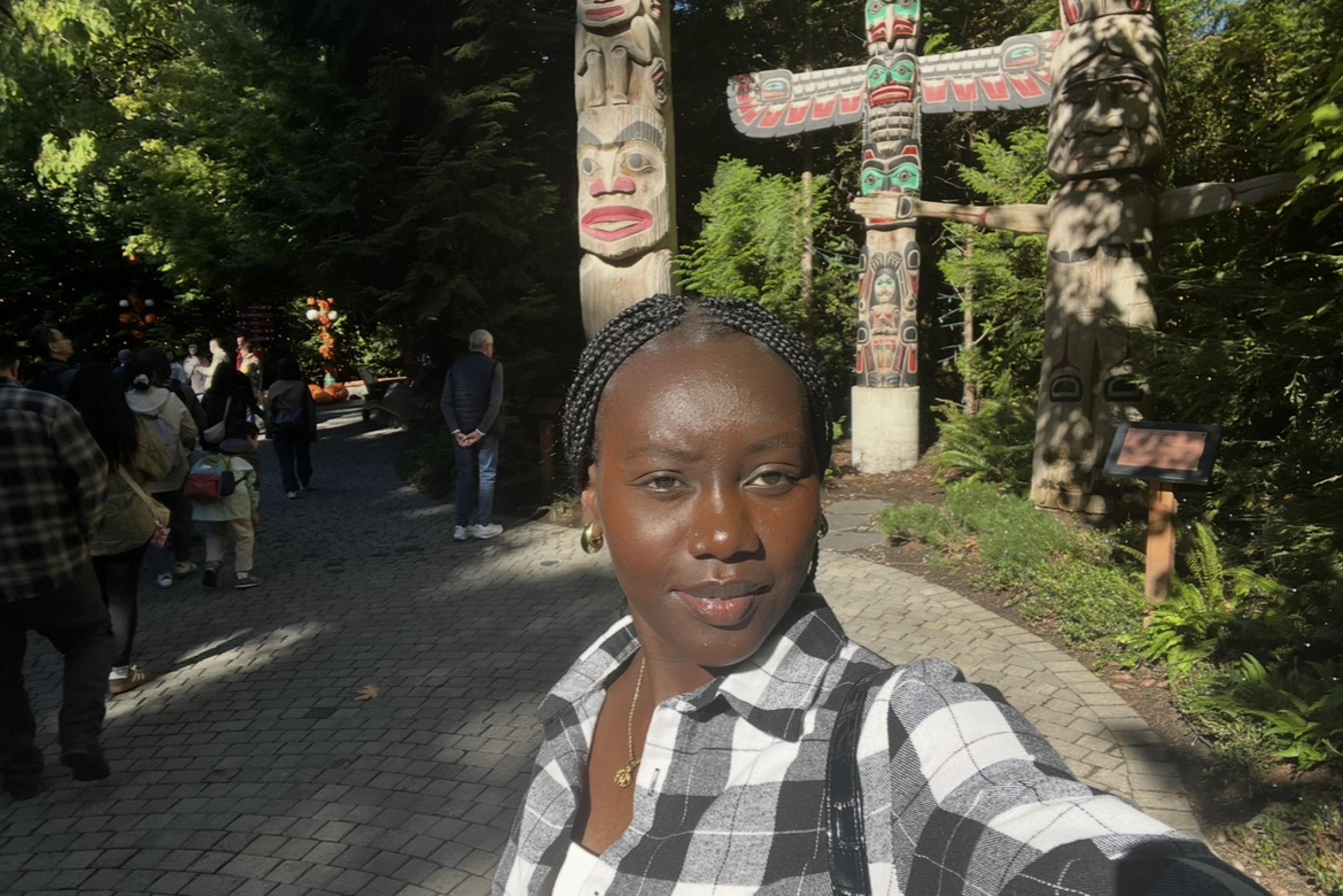 Kiru taking a selfie in front of a wooded area with totem poles. 
