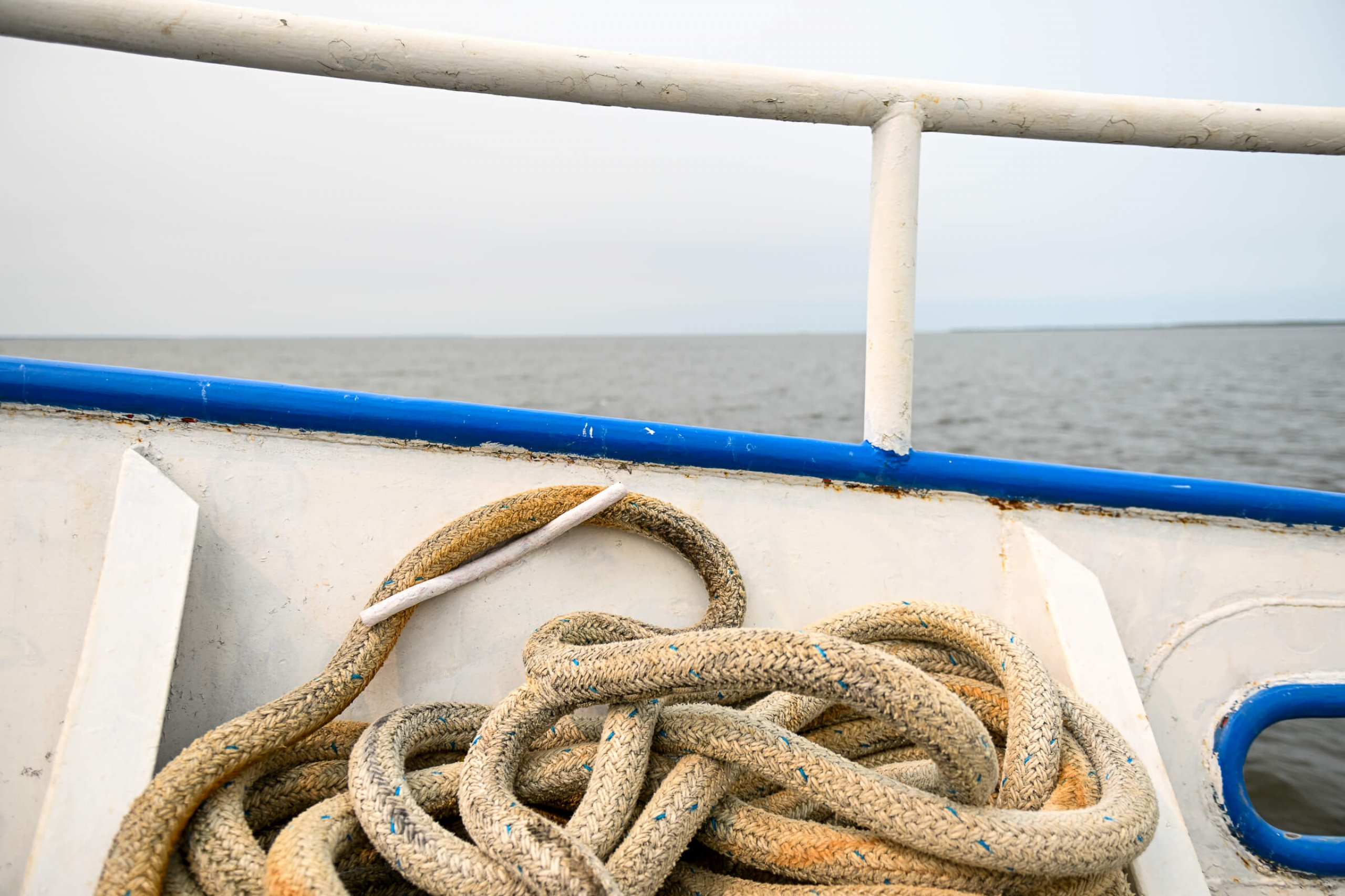 Close up image of a dirty rope on the deck of a boat with the lake stretching off in the background