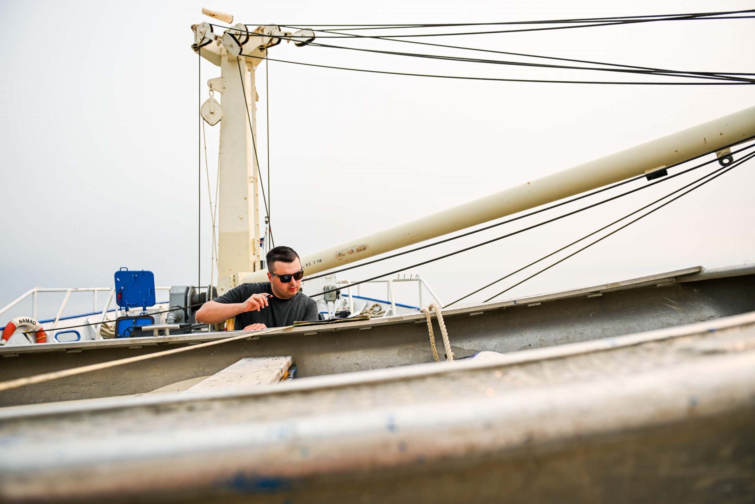 A man with sunglasses on the deck of a boat reading his notes