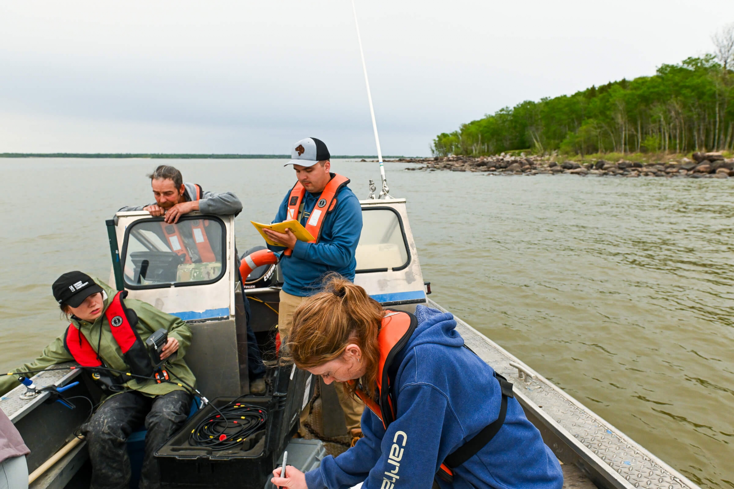 Researchers stand in a small boat on the lake writing down their observations