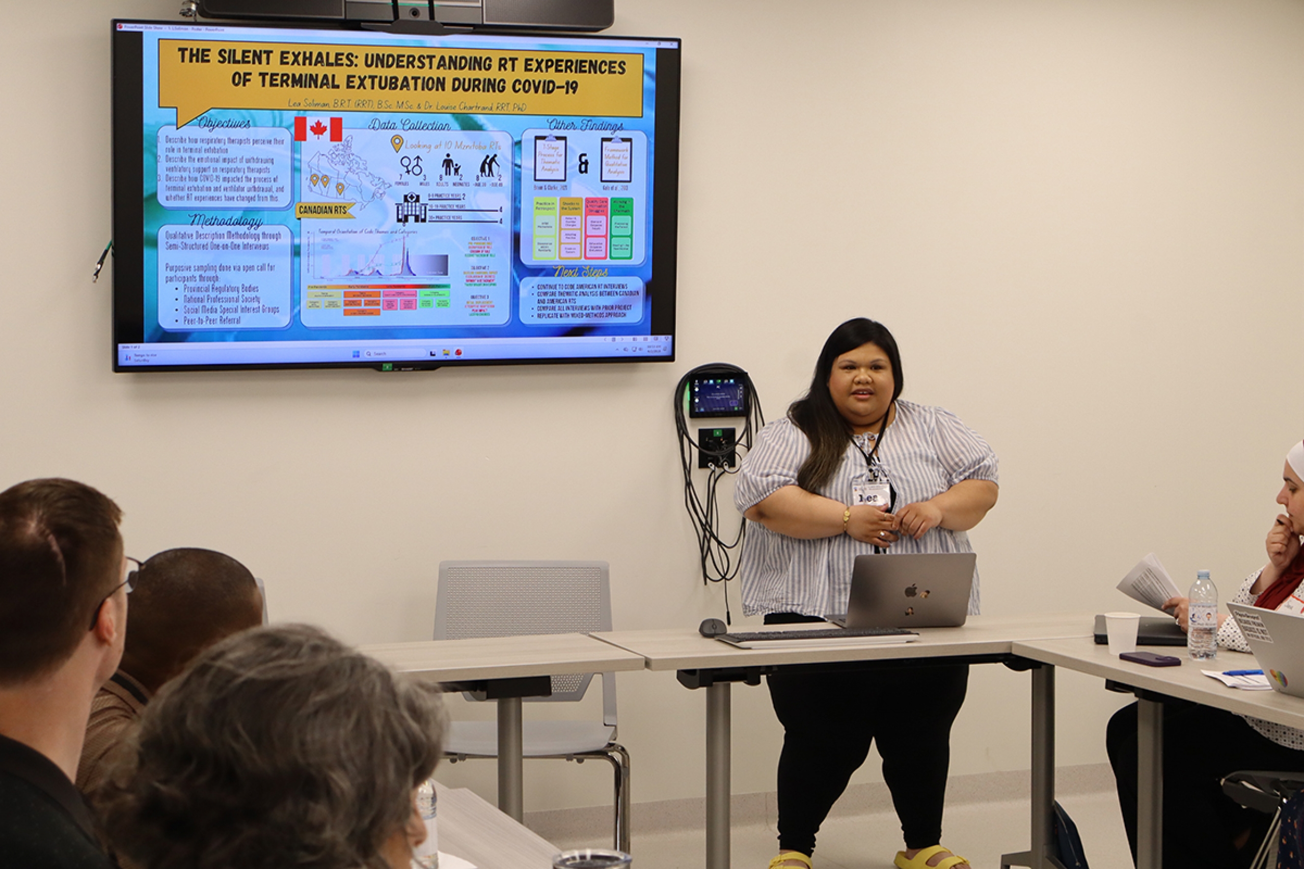Lea Soliman in front of a screen showing her research project, titled "The Silent Exhales: Understanding RT Experiences of Terminal Extubation During COVID-19."
