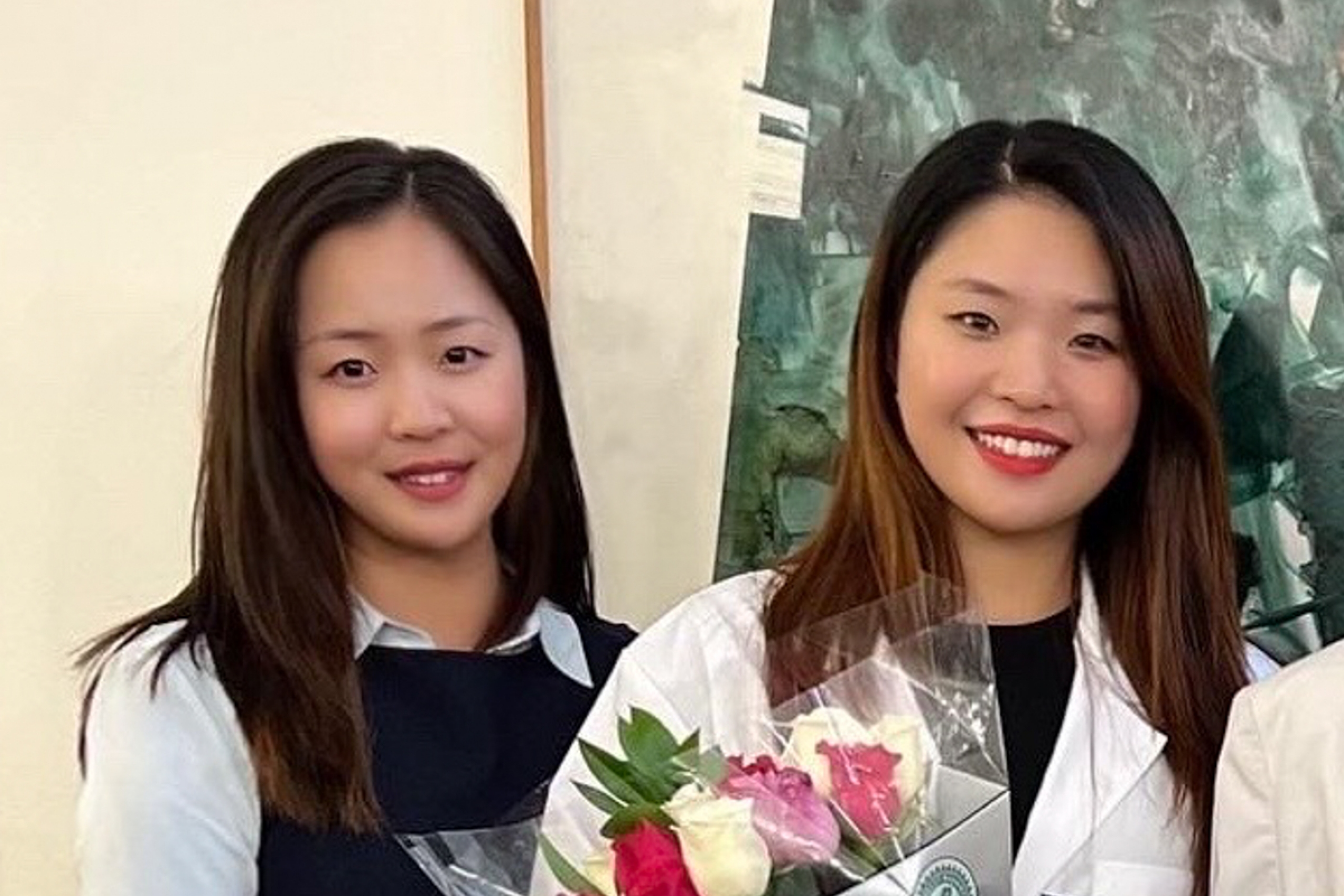 Two people smile at the camera; the person on the right holds a bouquet of flowers.