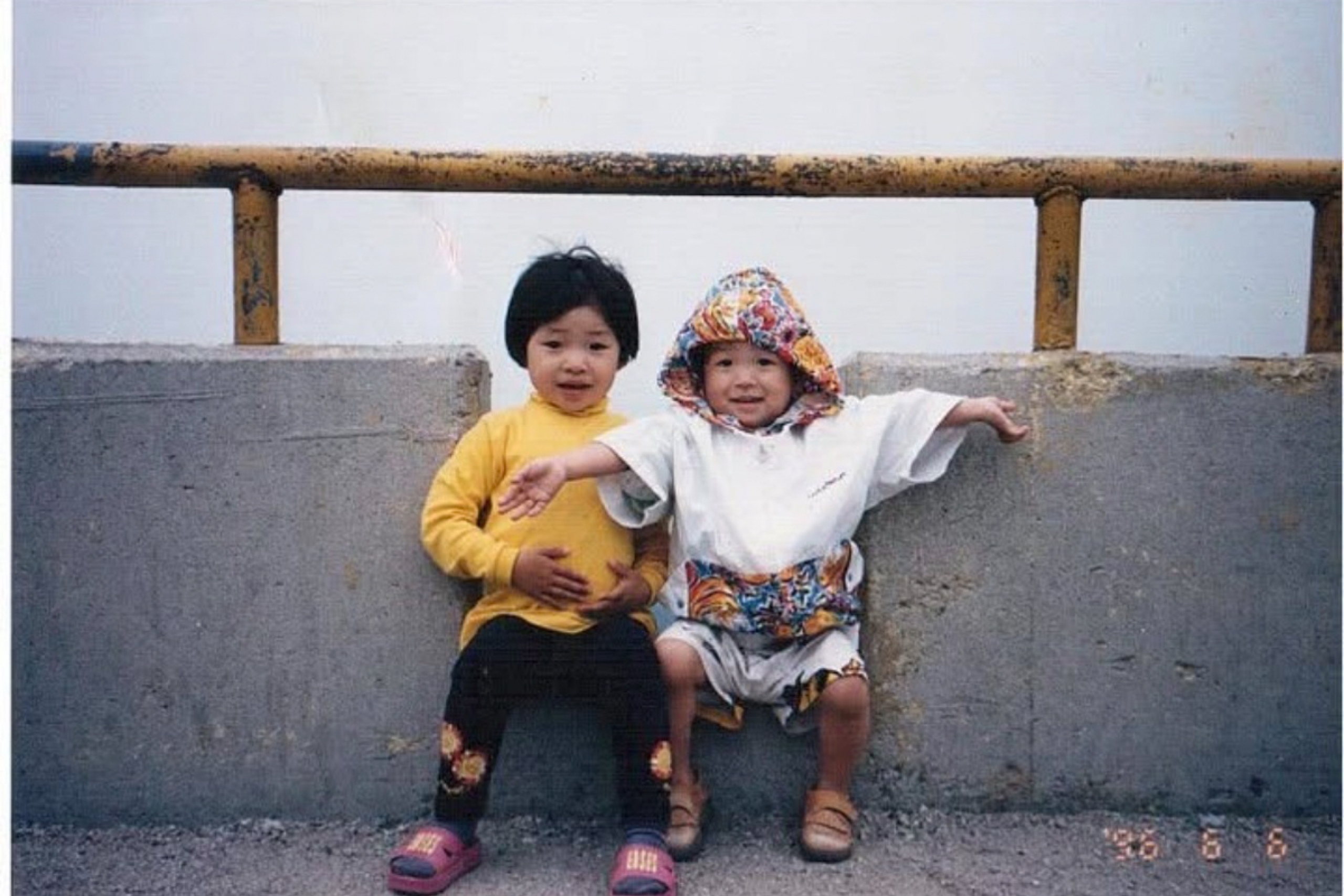 Two small children sit by a bridge and smile at the camera.