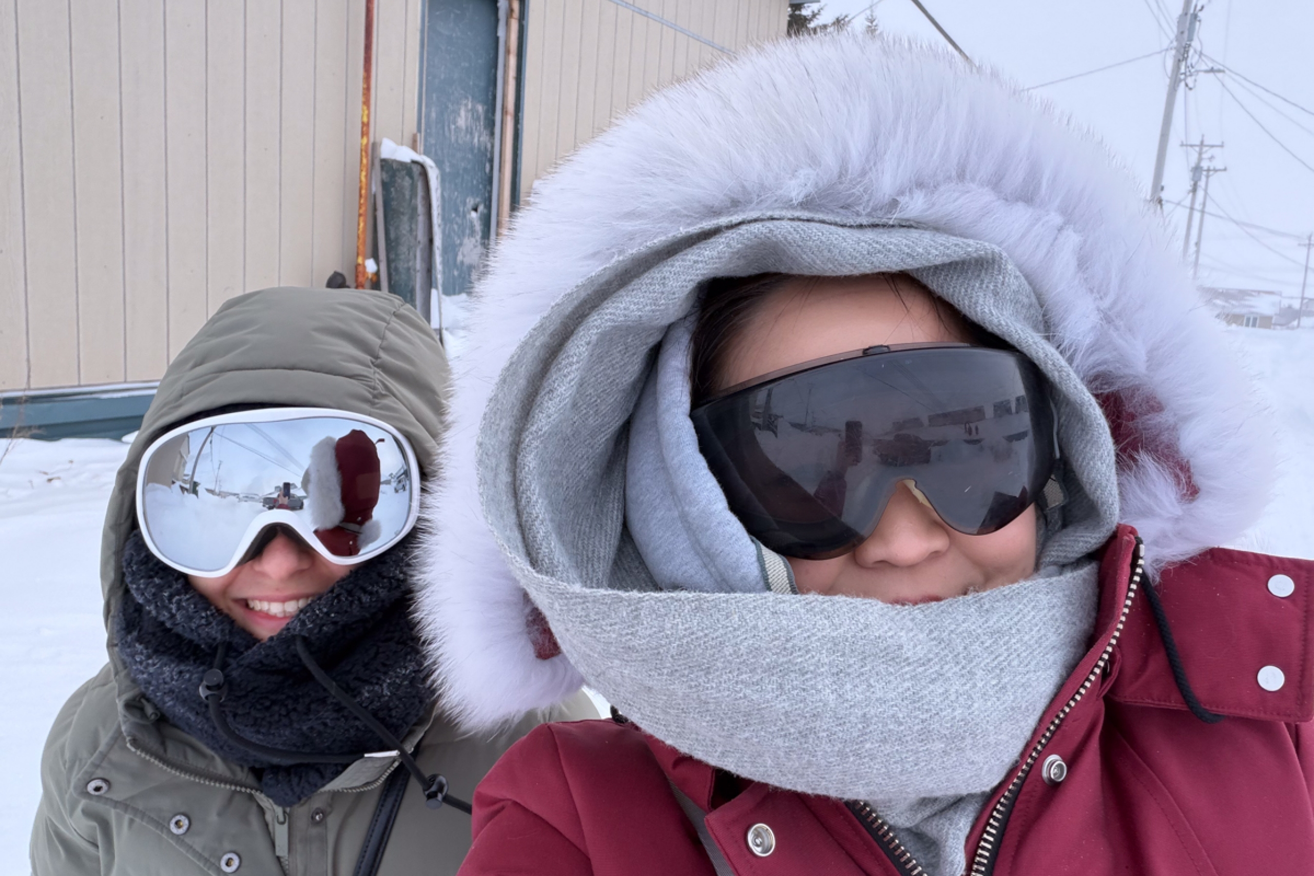 Two people in full winter gear with goggles smile at the camera.
