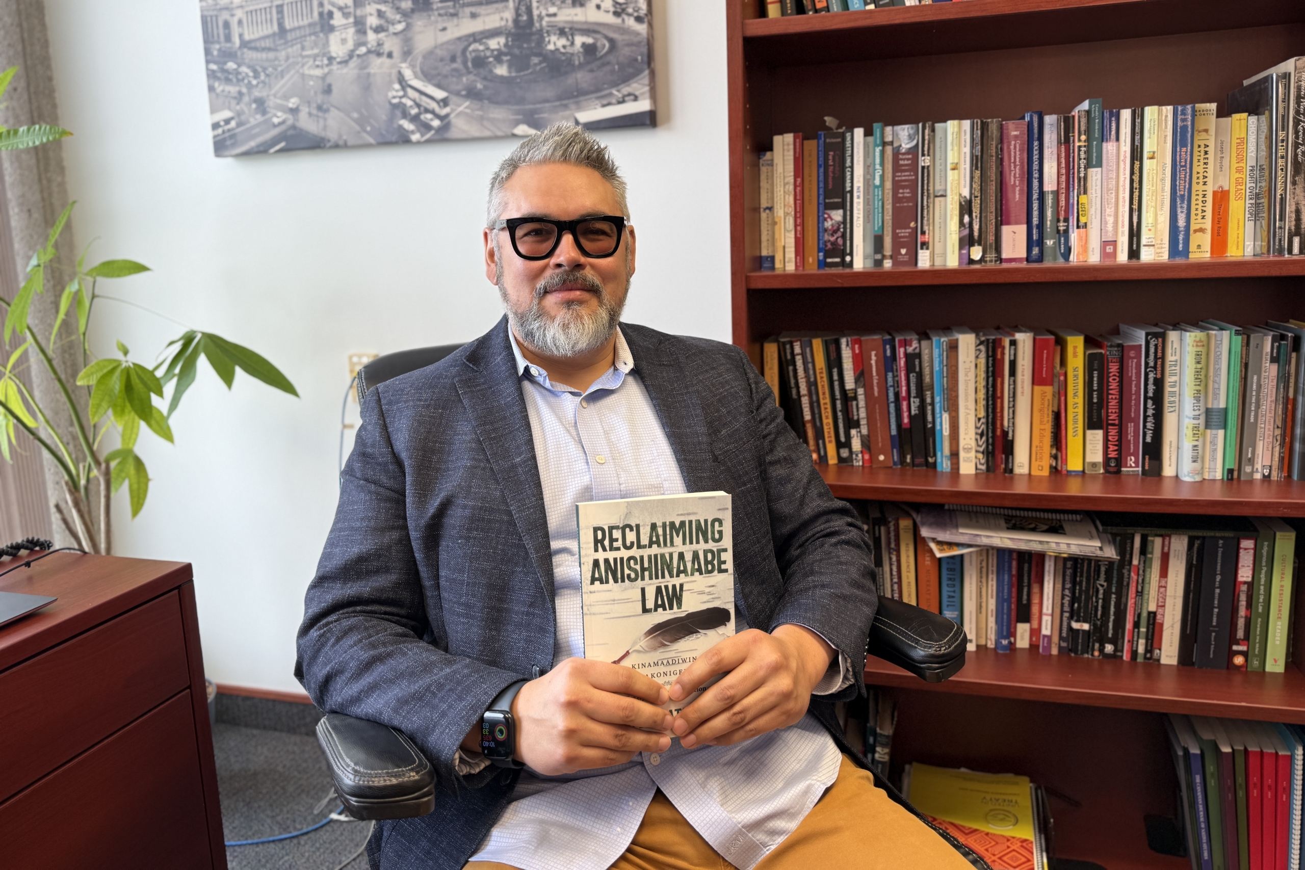 Man holds book, smiling while seated in front of bookcase