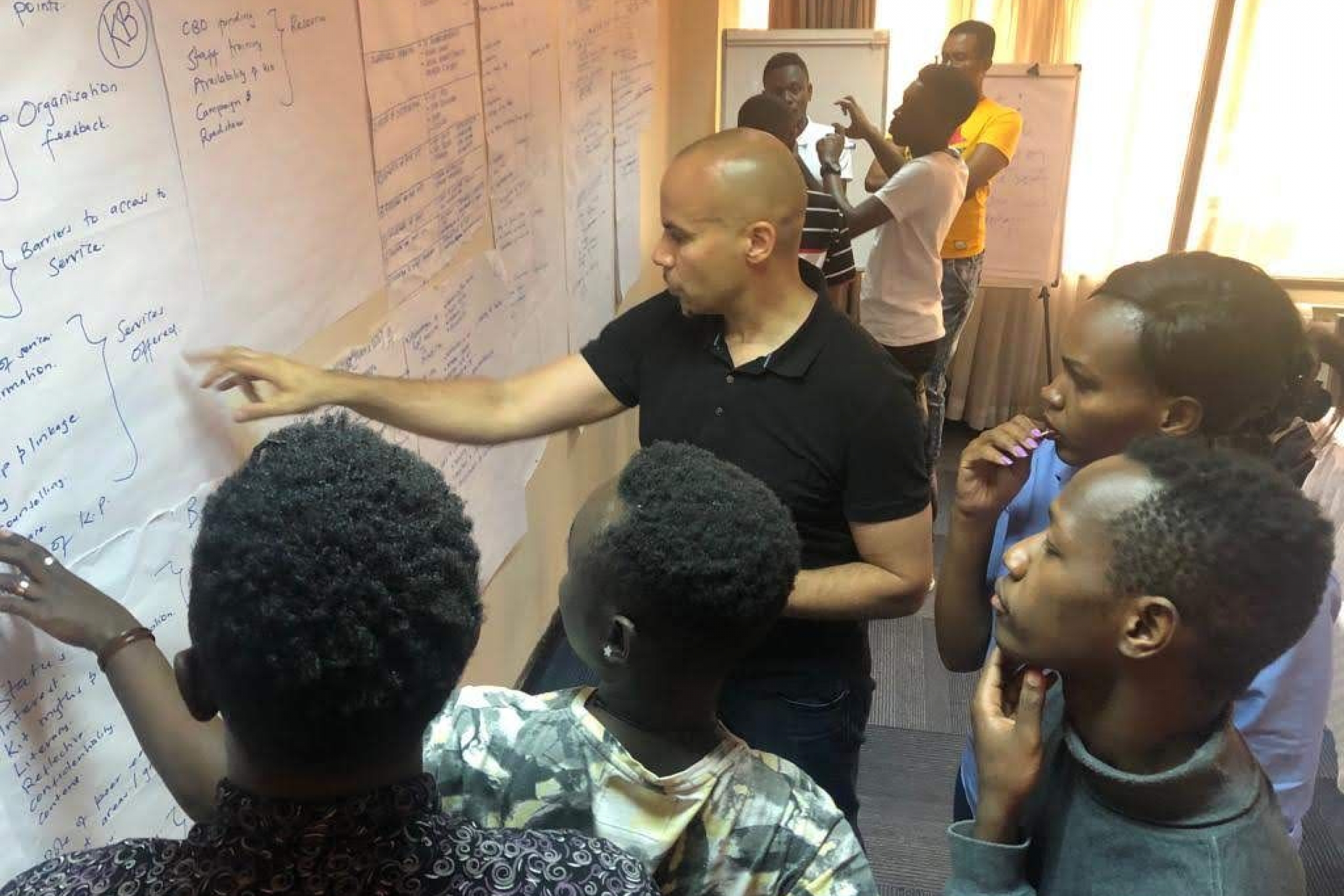 Five people read and analyze research data displayed on a wall.