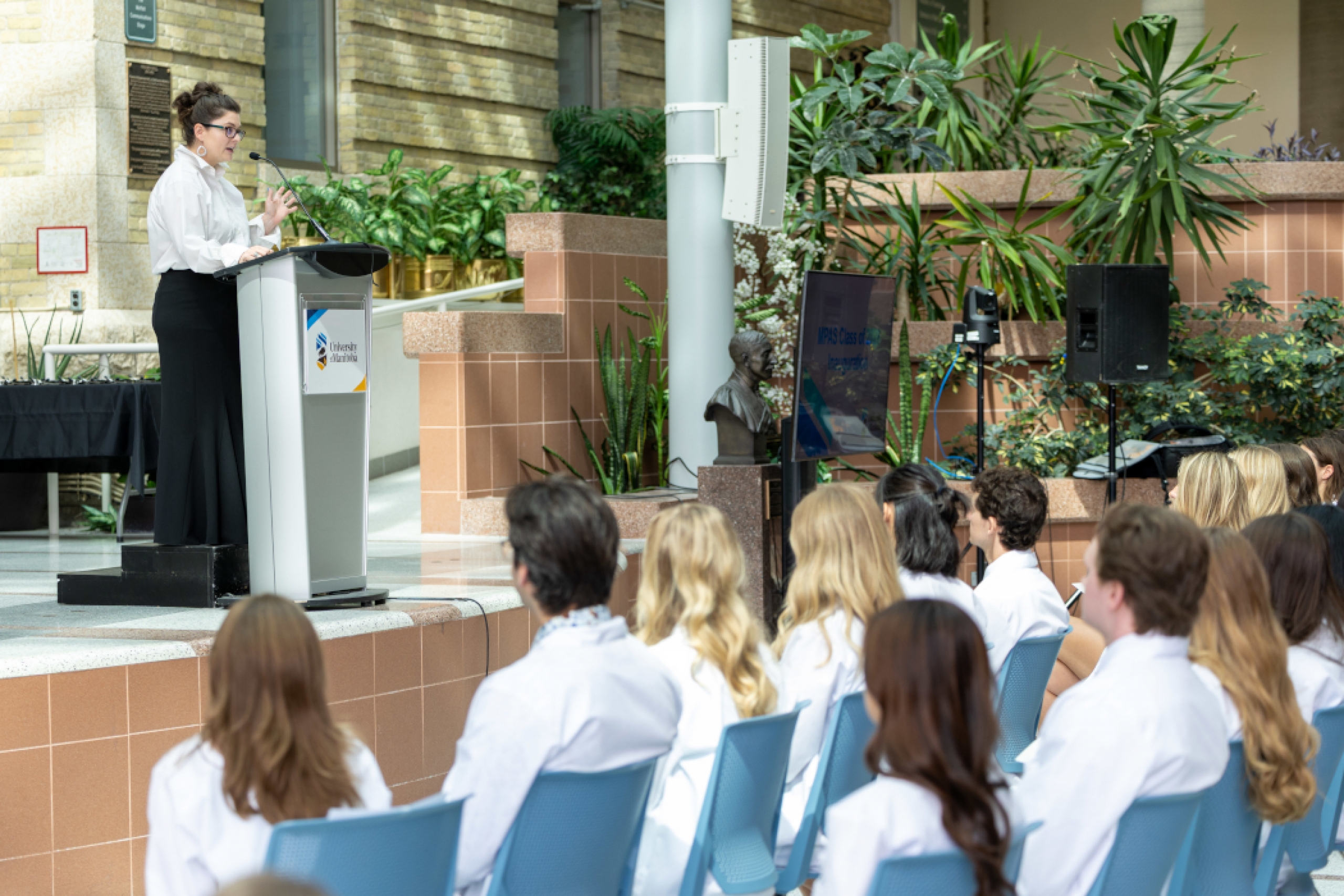 Rebecca Mueller speaks at a lectern on a stage. Students are seated in front of her.