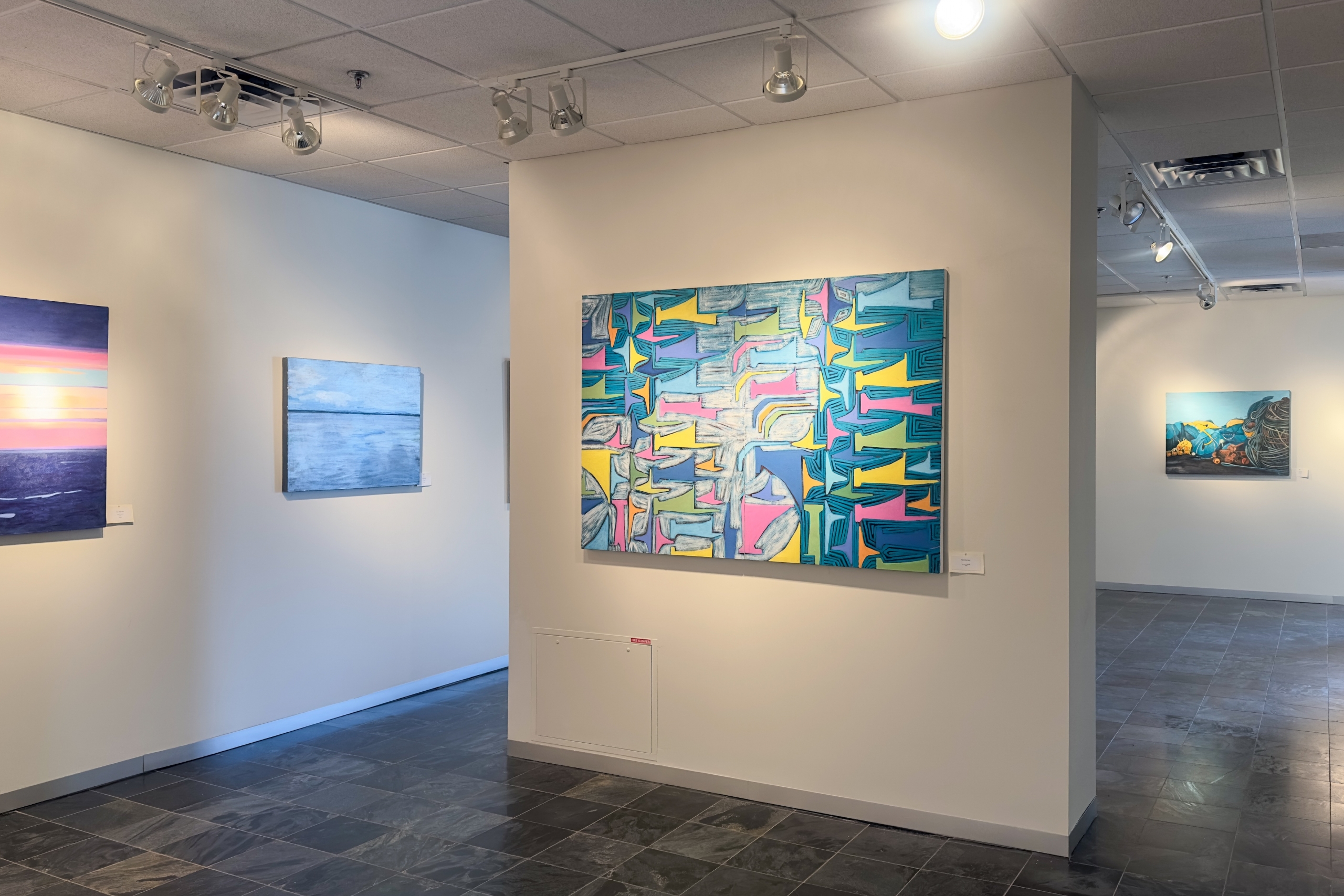 Gallery installation view featuring large colourful abstract paintings on white walls under track lighting.