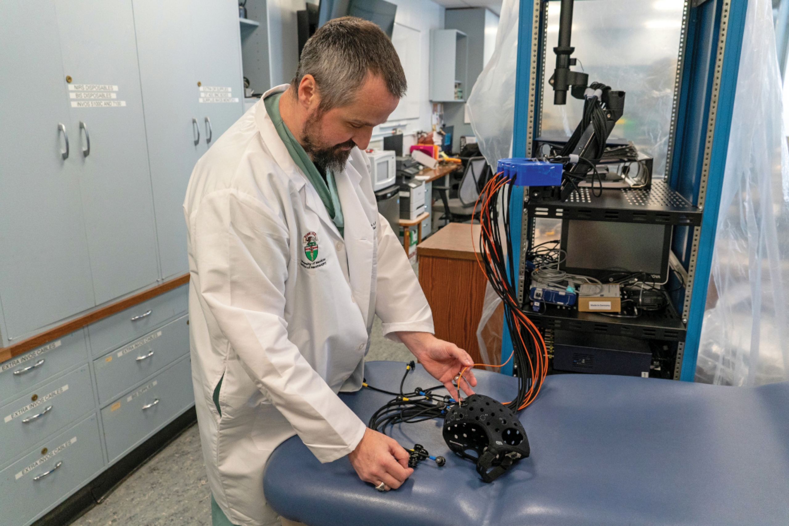 A researcher in his lab works with a monitoring device that is connected to several wires.