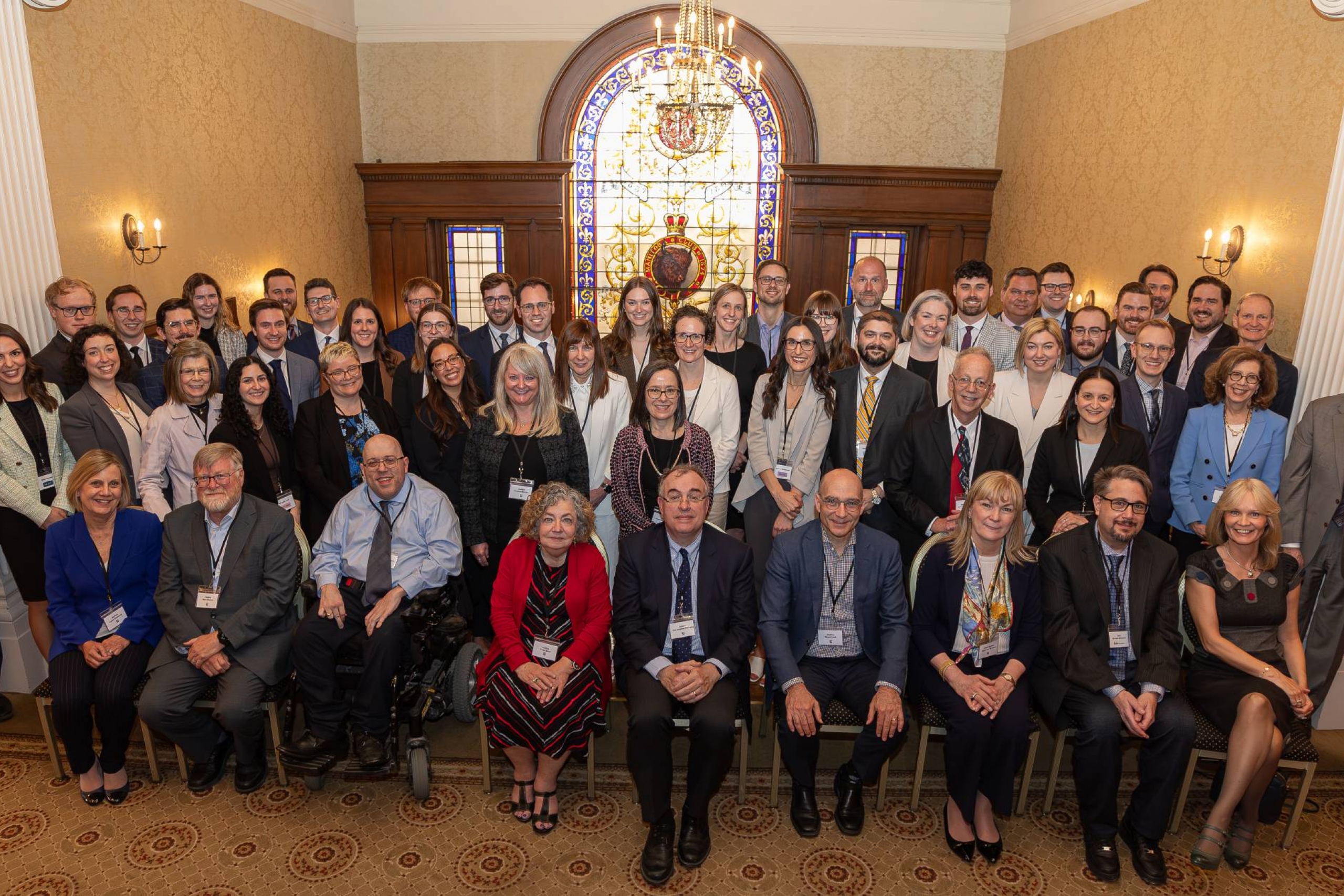 Two dozen people smile at the camera in a historical room with floor mosaics and stained glass.
