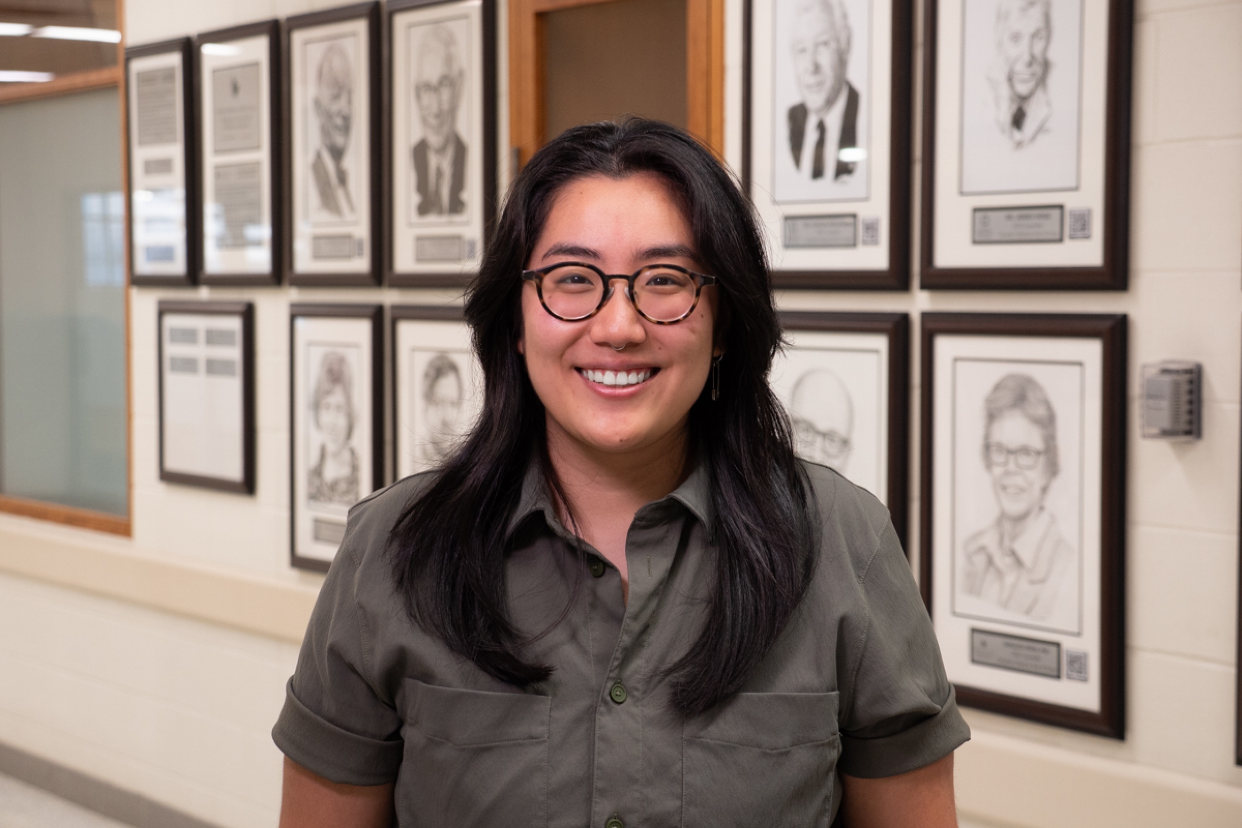 A person standing in front of a wall with framed photos of ten people.