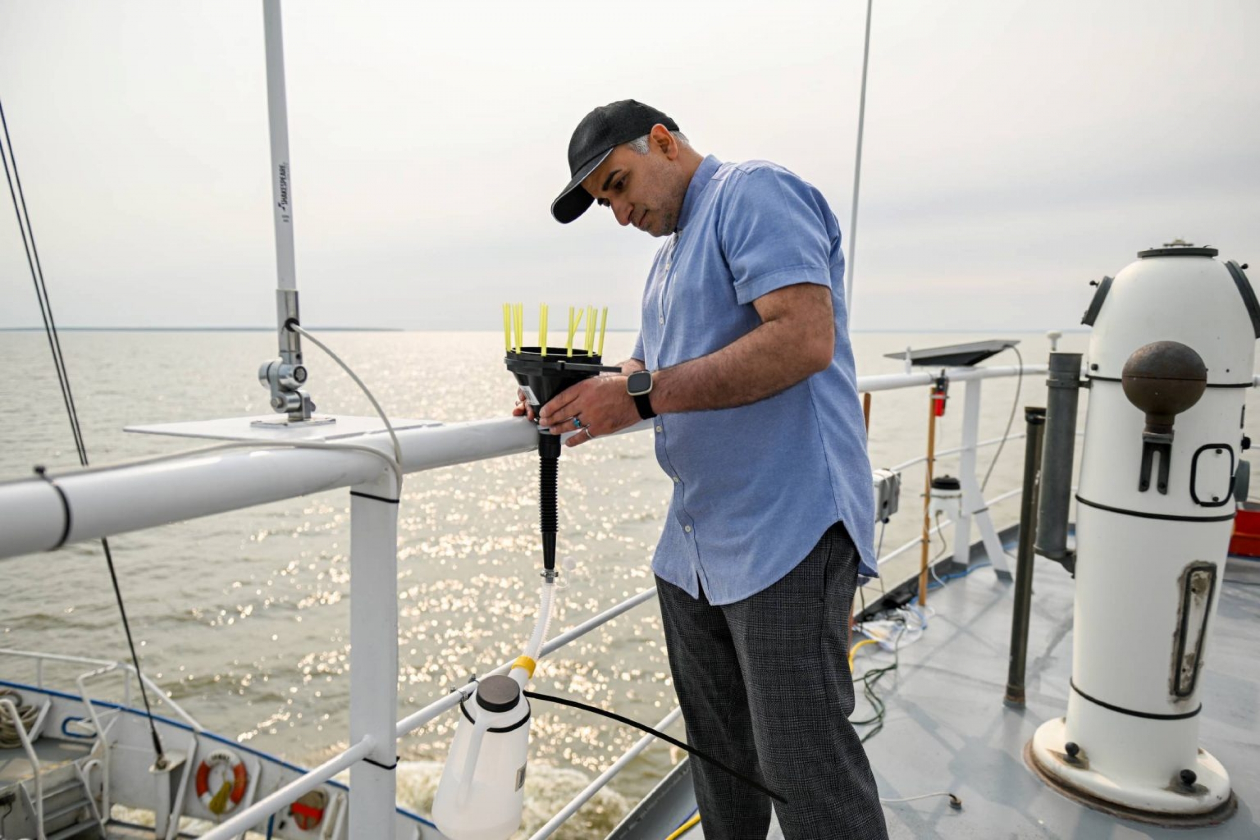 A man in a baseball cap (Dr. Masoud Goharrokhi) inspects instruments on the deck of a boat