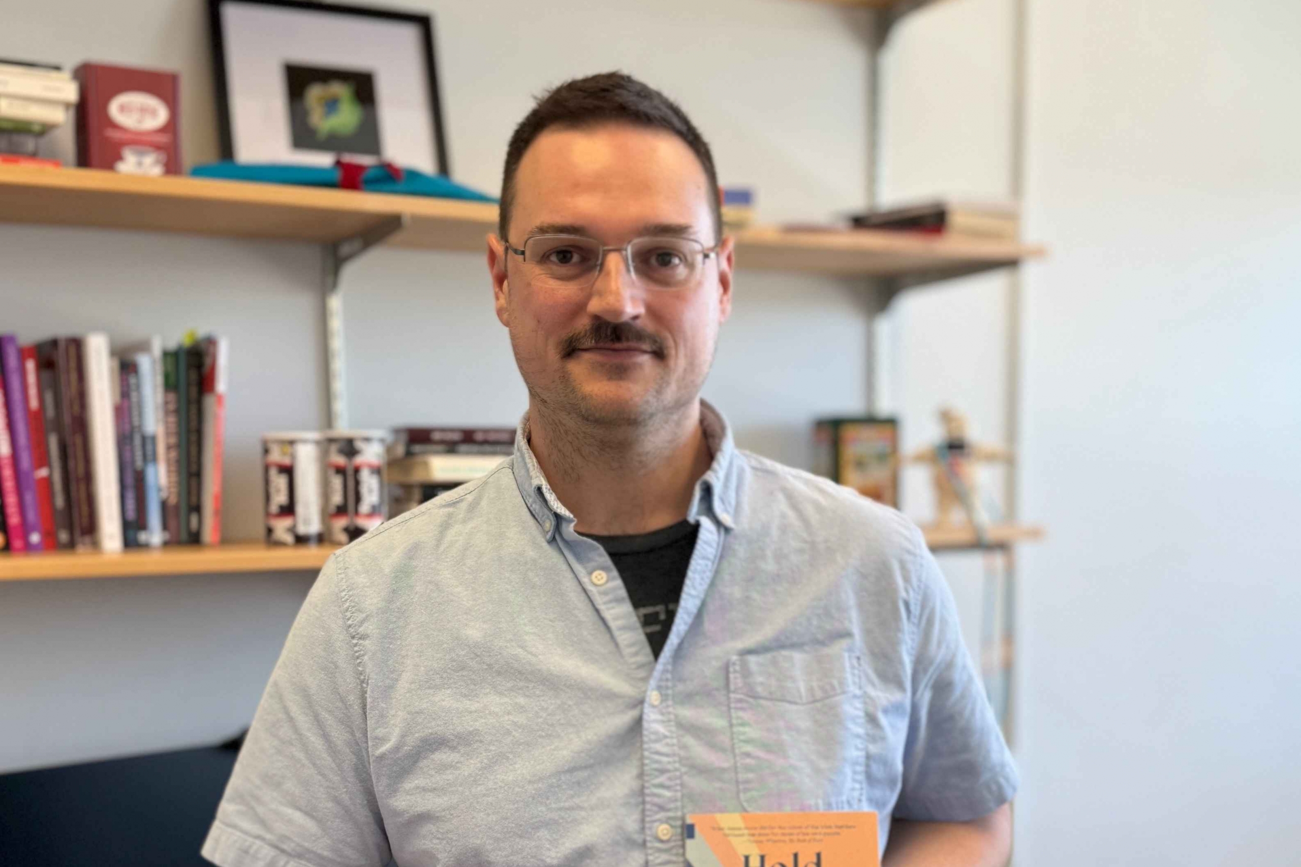 Matthew holds his novel and smiles in his office.