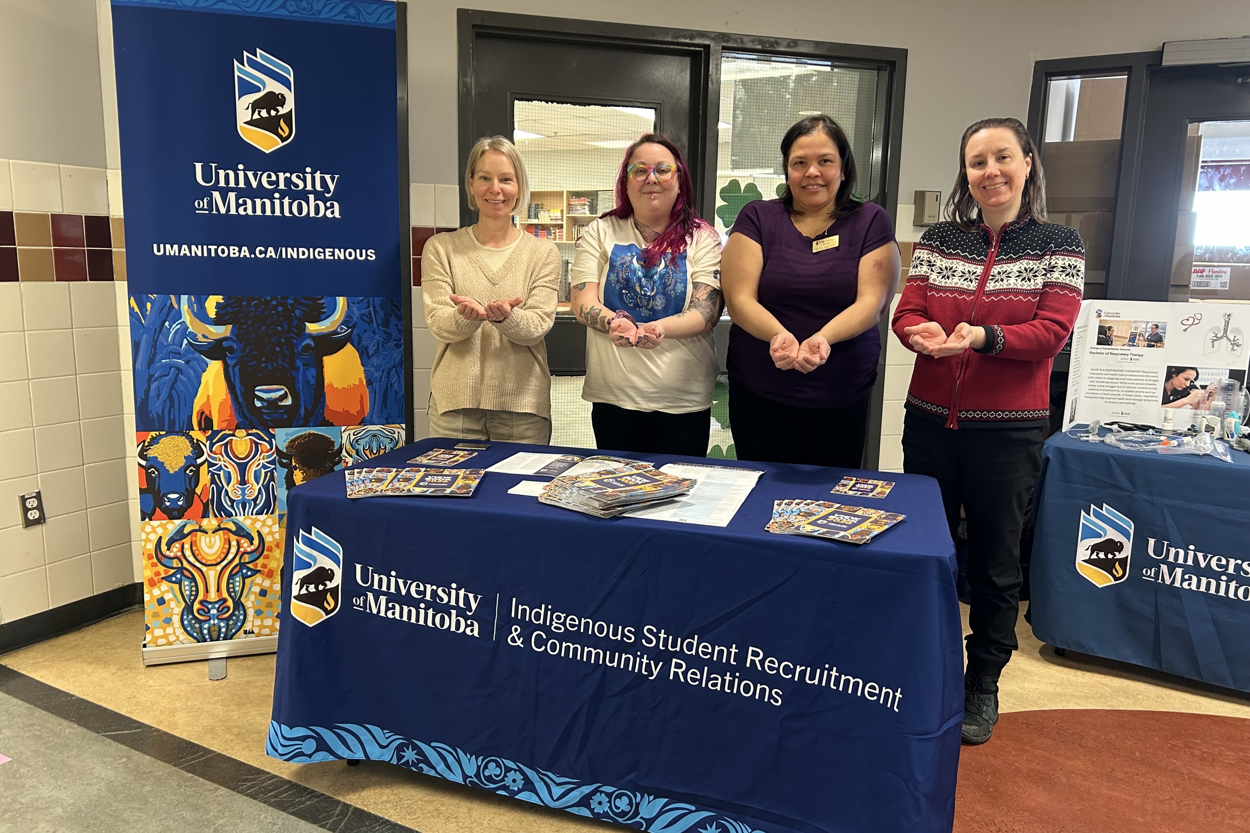 Four people striking the Give to Gain pose in a UM recruitment booth.
