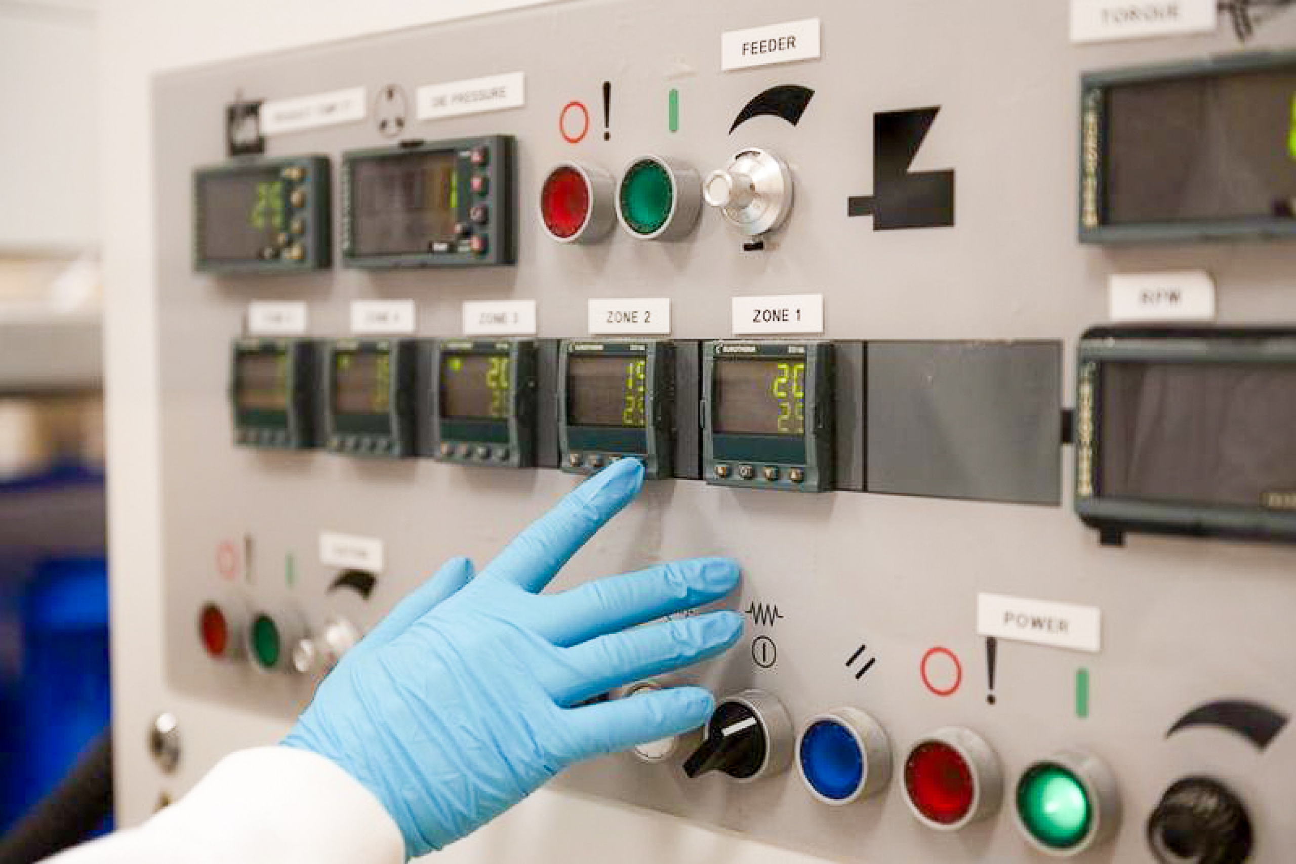 A gloved hand presses buttons on machinery