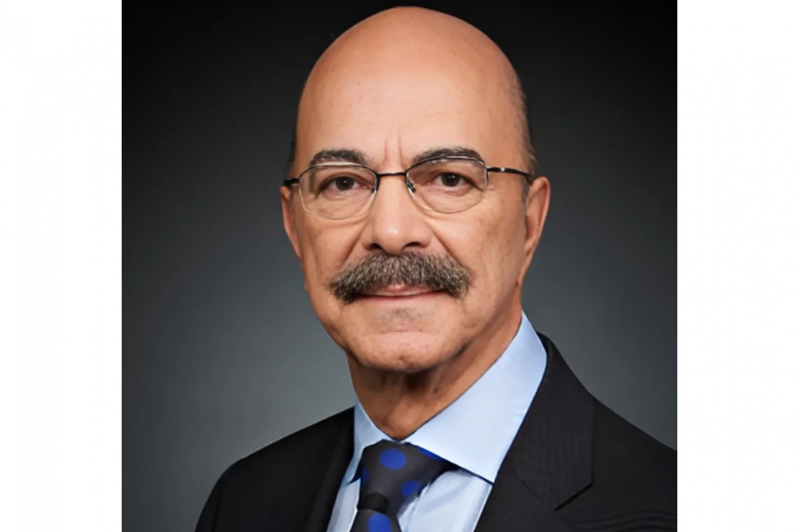 Man in glasses and suit with a mustache, posed against a dark background