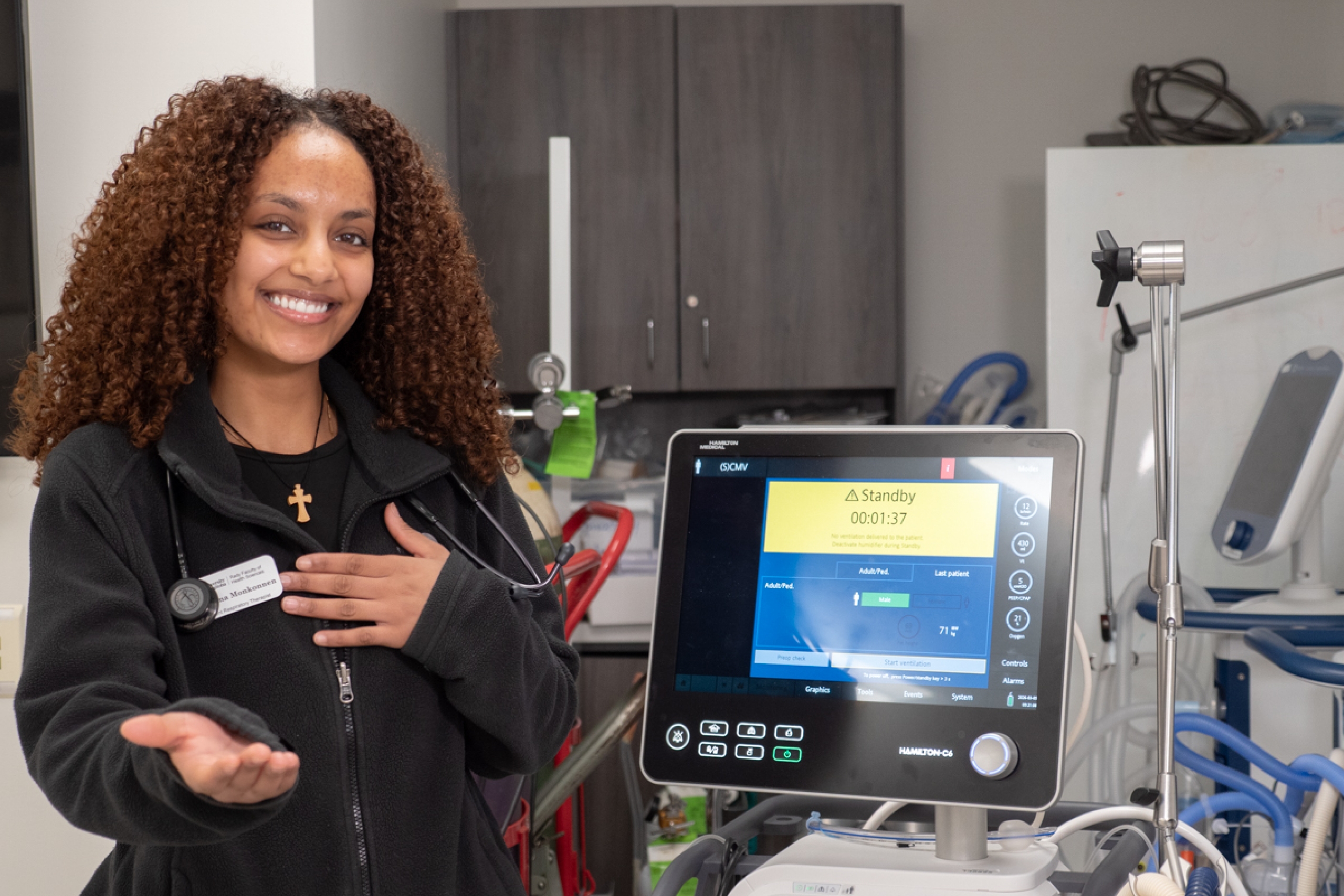 A person strikes the Give to Gain pose, in a room with respiratory therapy equipment.