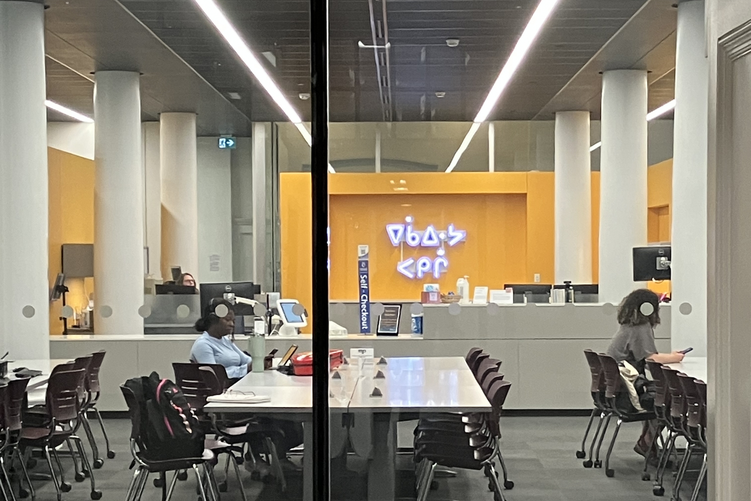 A neon sign in Cree displayed on back wall of music library