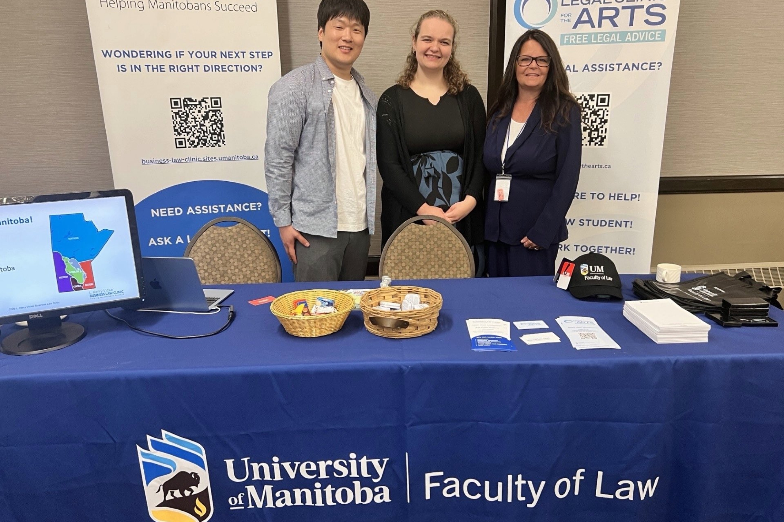 three people stand and smile at a Faculty of Law booth at a tradeshow