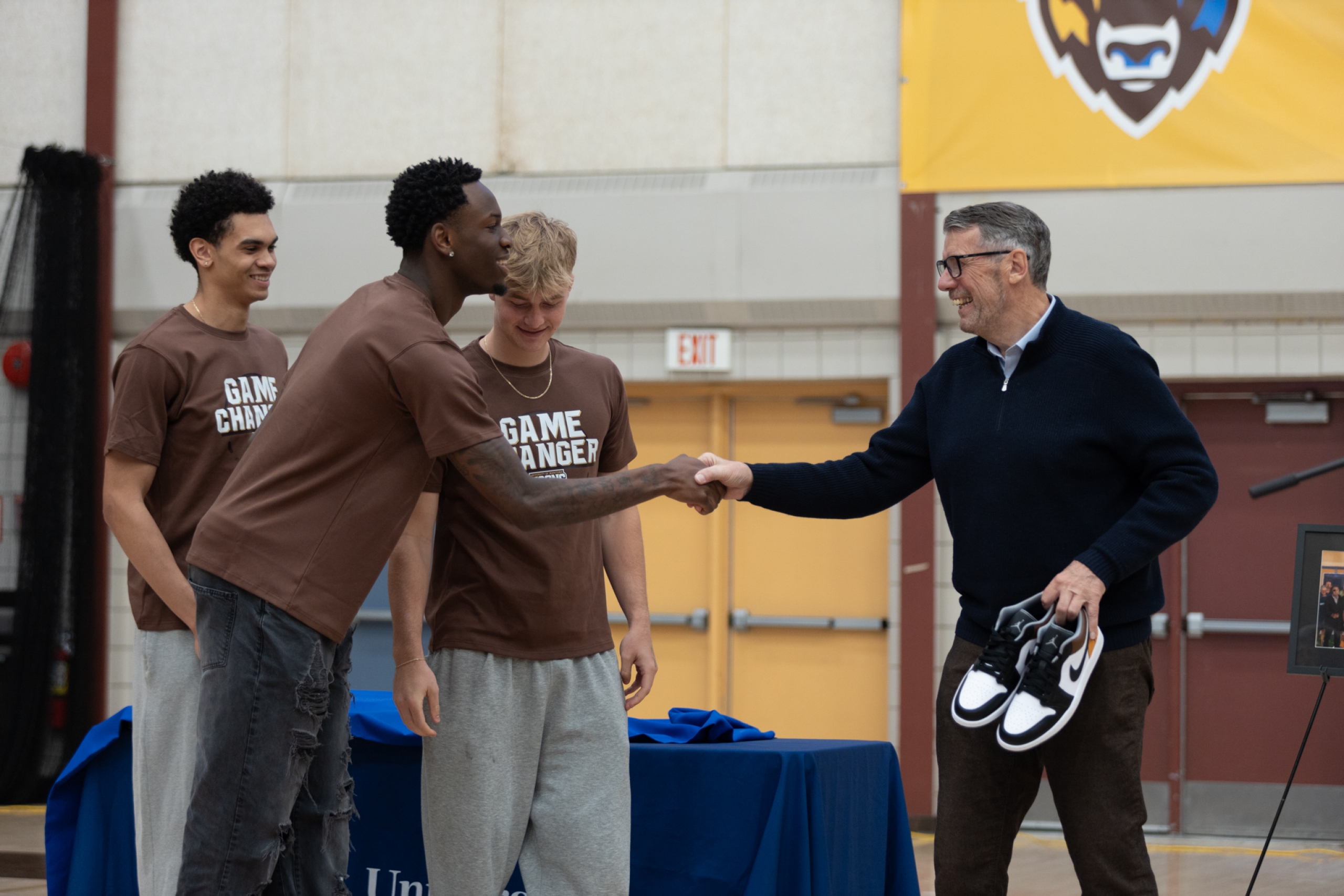 three men's basketball players present a pair of shoes to John Loewen