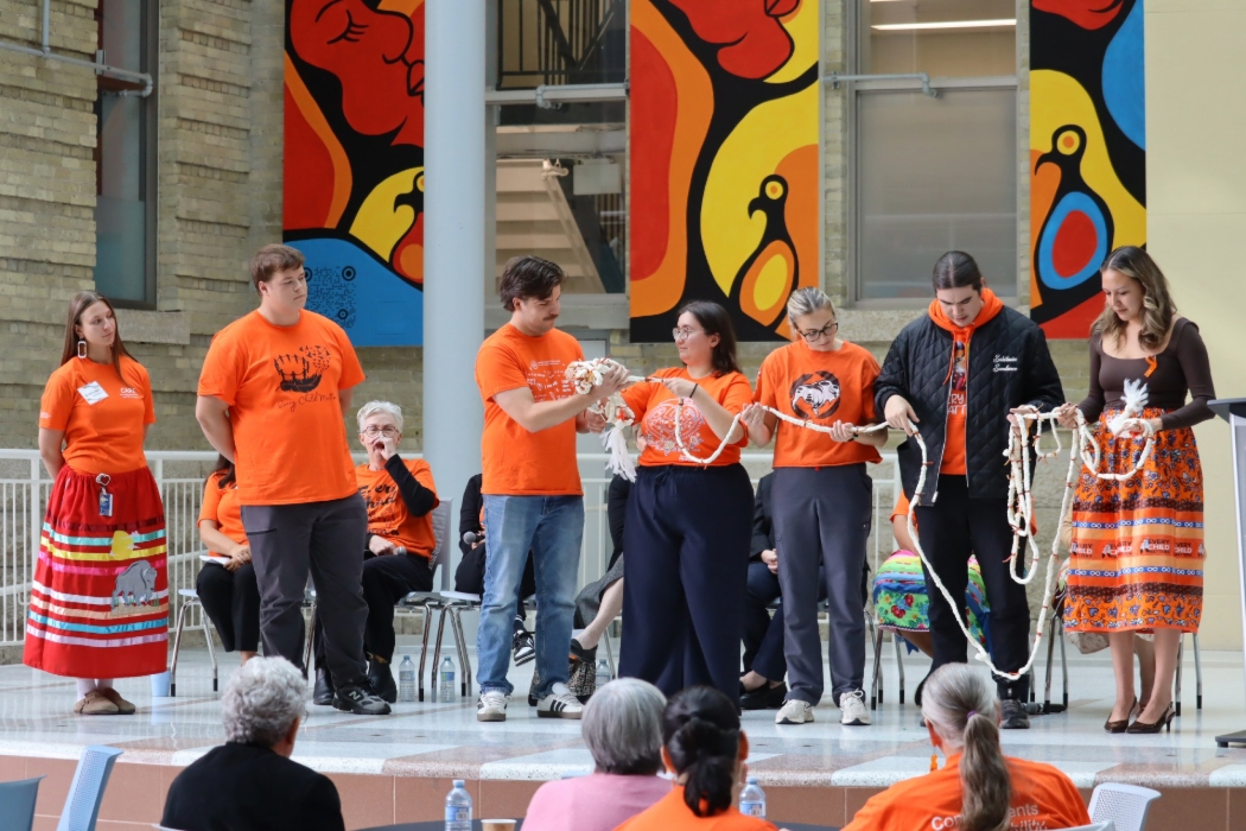 Students in orange shirts sharing the braid on stage