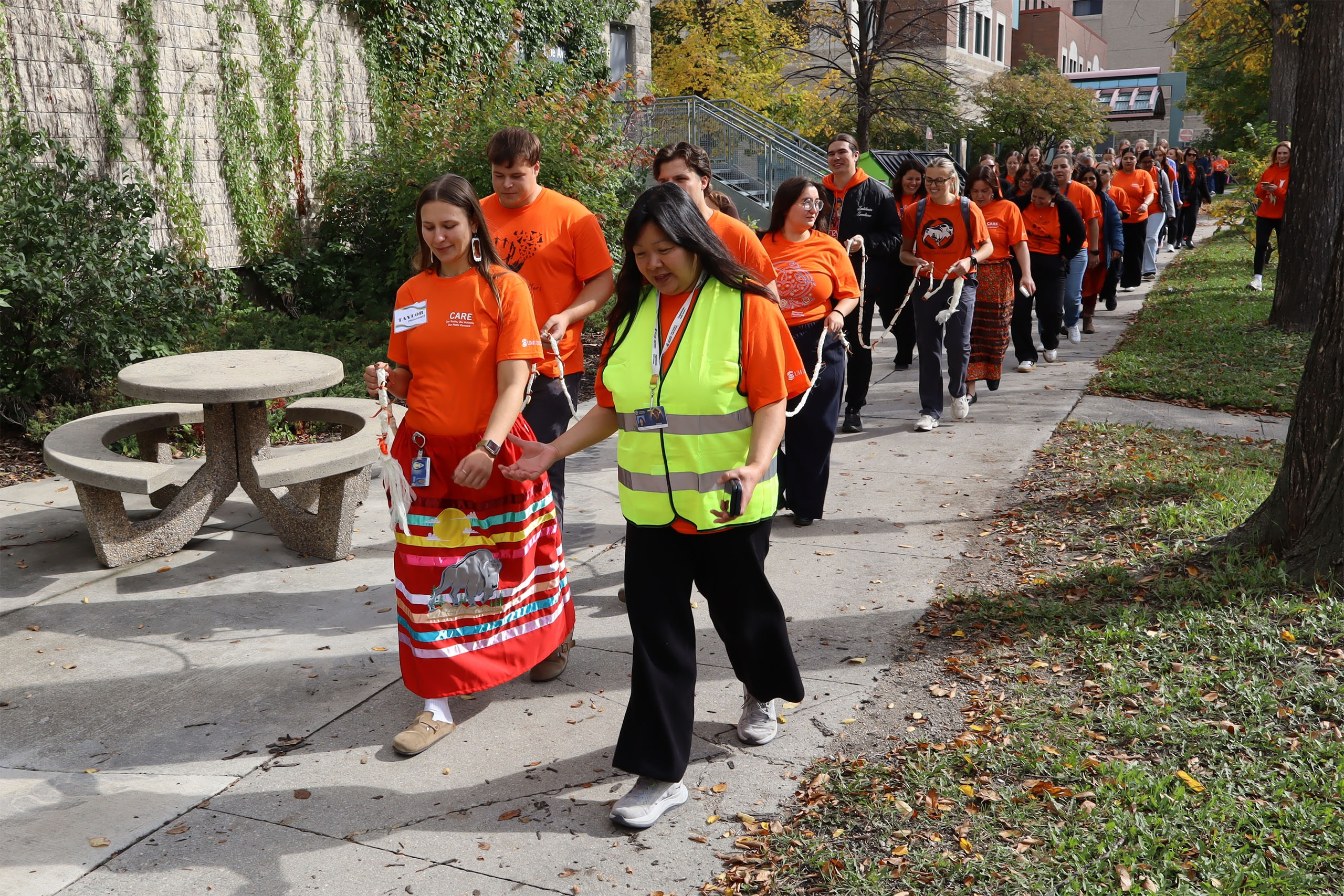 A group of people in orange shirts walking on the sidewalk.