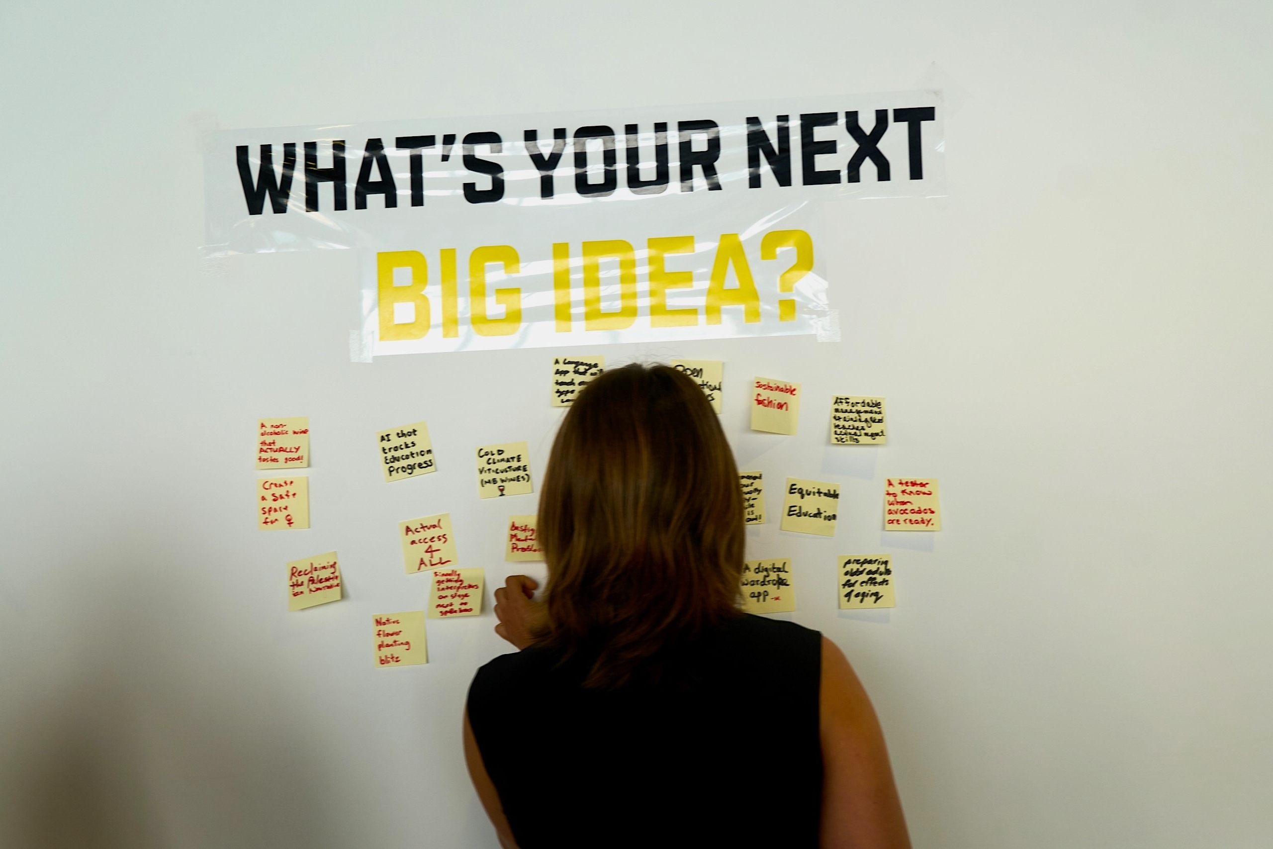 A person adds yellow post-it notes to a white board with the words "What's your next big idea?"