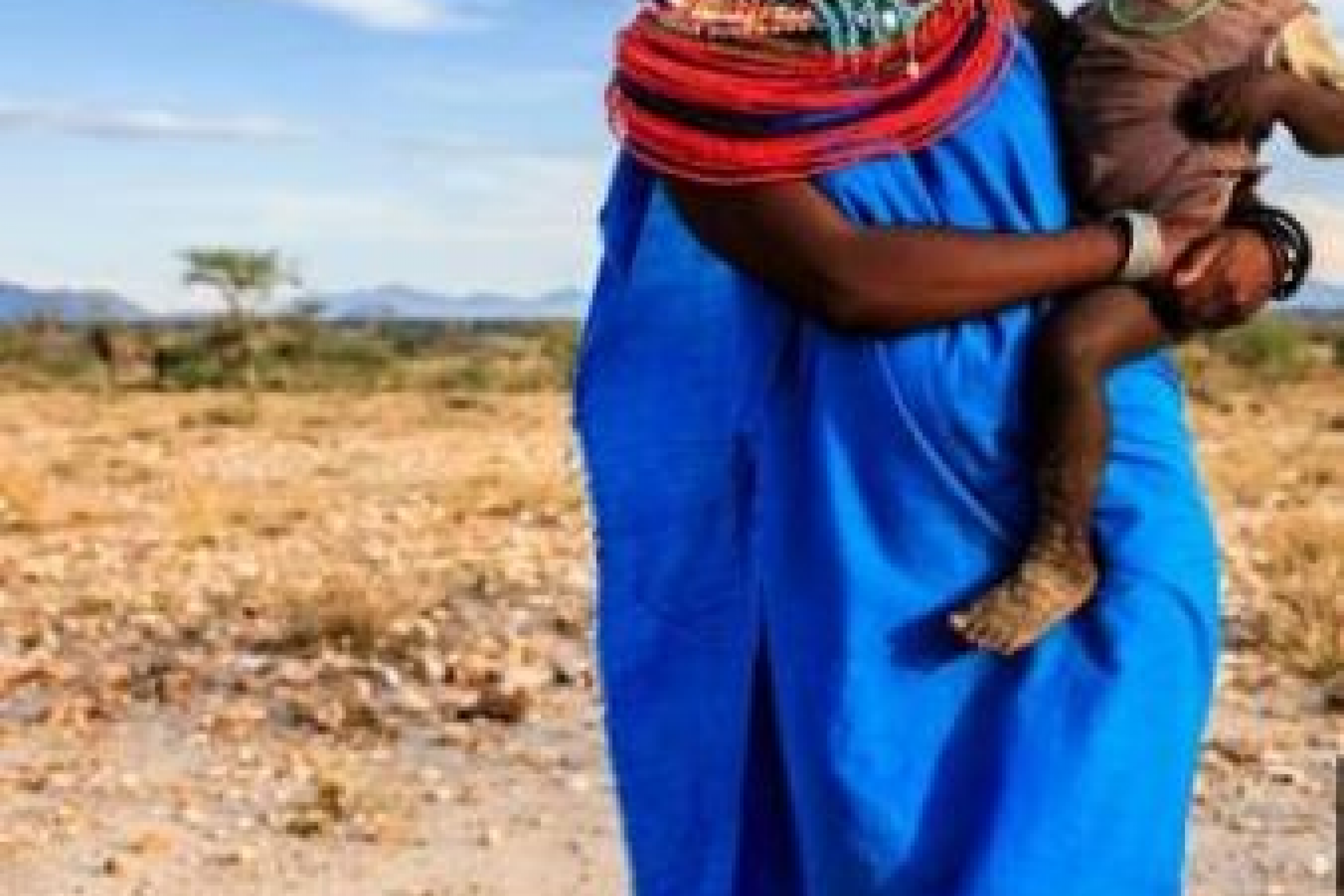A Nigerian woman in a blue dress holds her baby on her hip