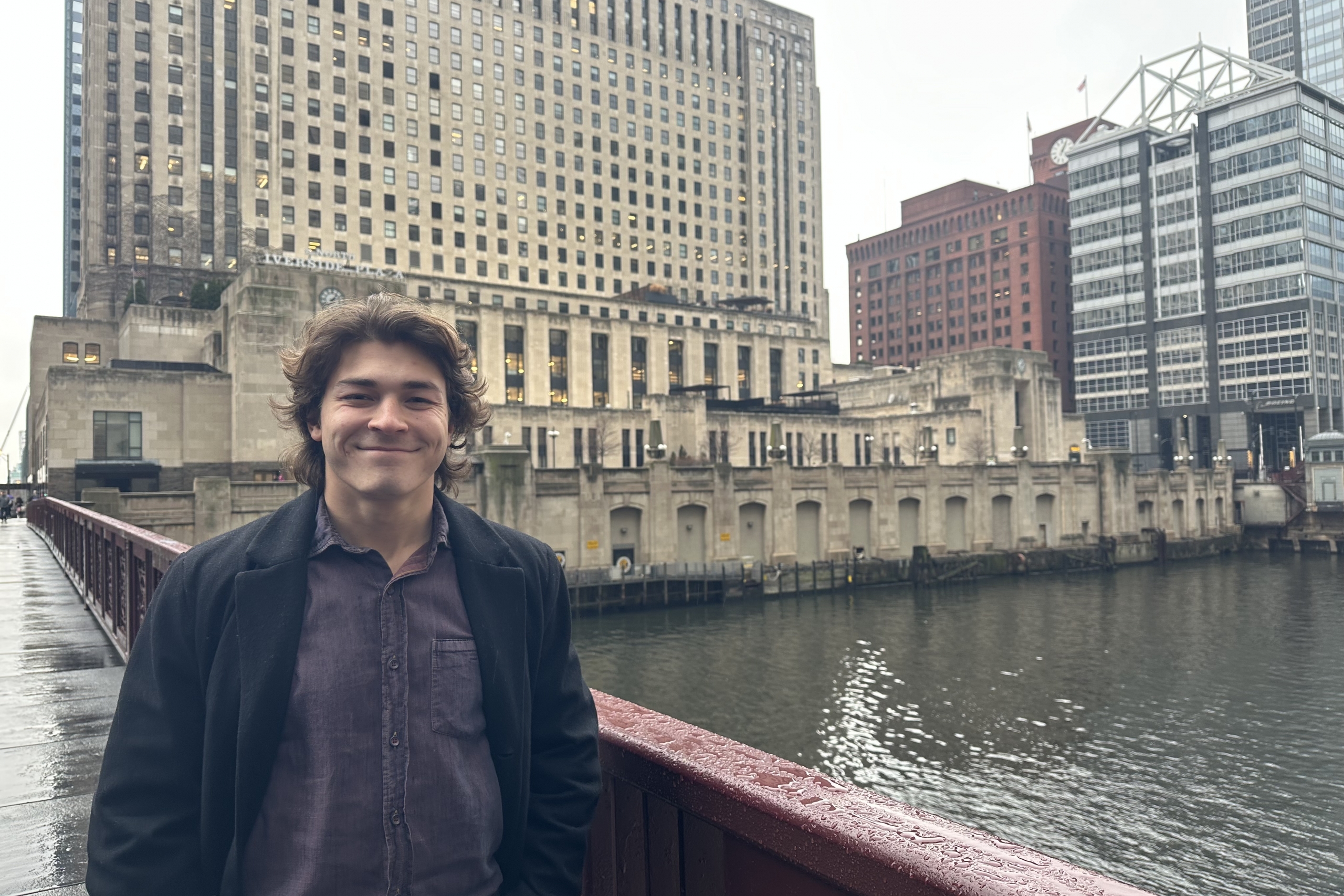 Person standing on a bridge with a cityscape waterfront behind them.